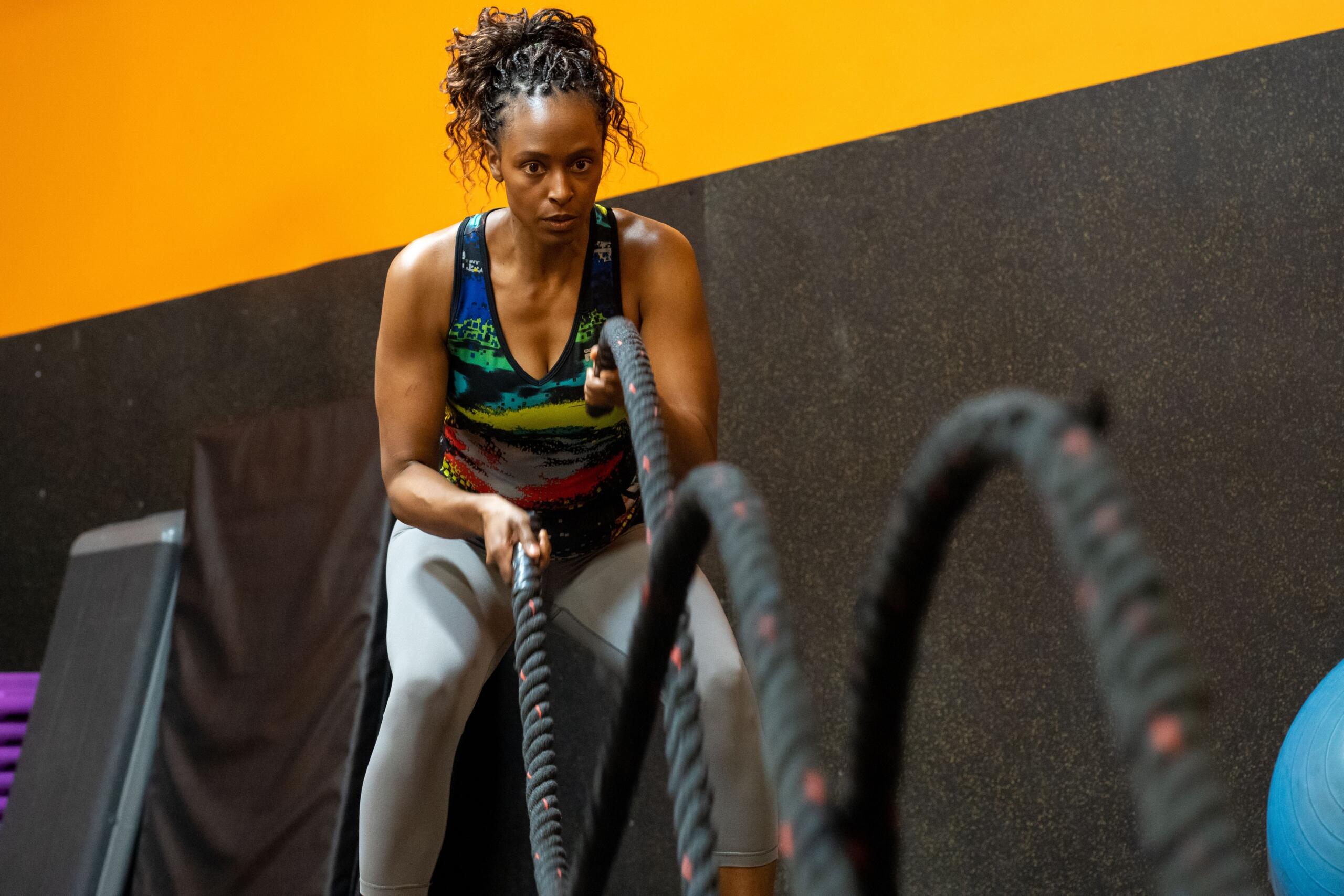 A woman uses battle ropes during a high-intensity workout in a gym, creating powerful waves while building strength and cardiovascular endurance.