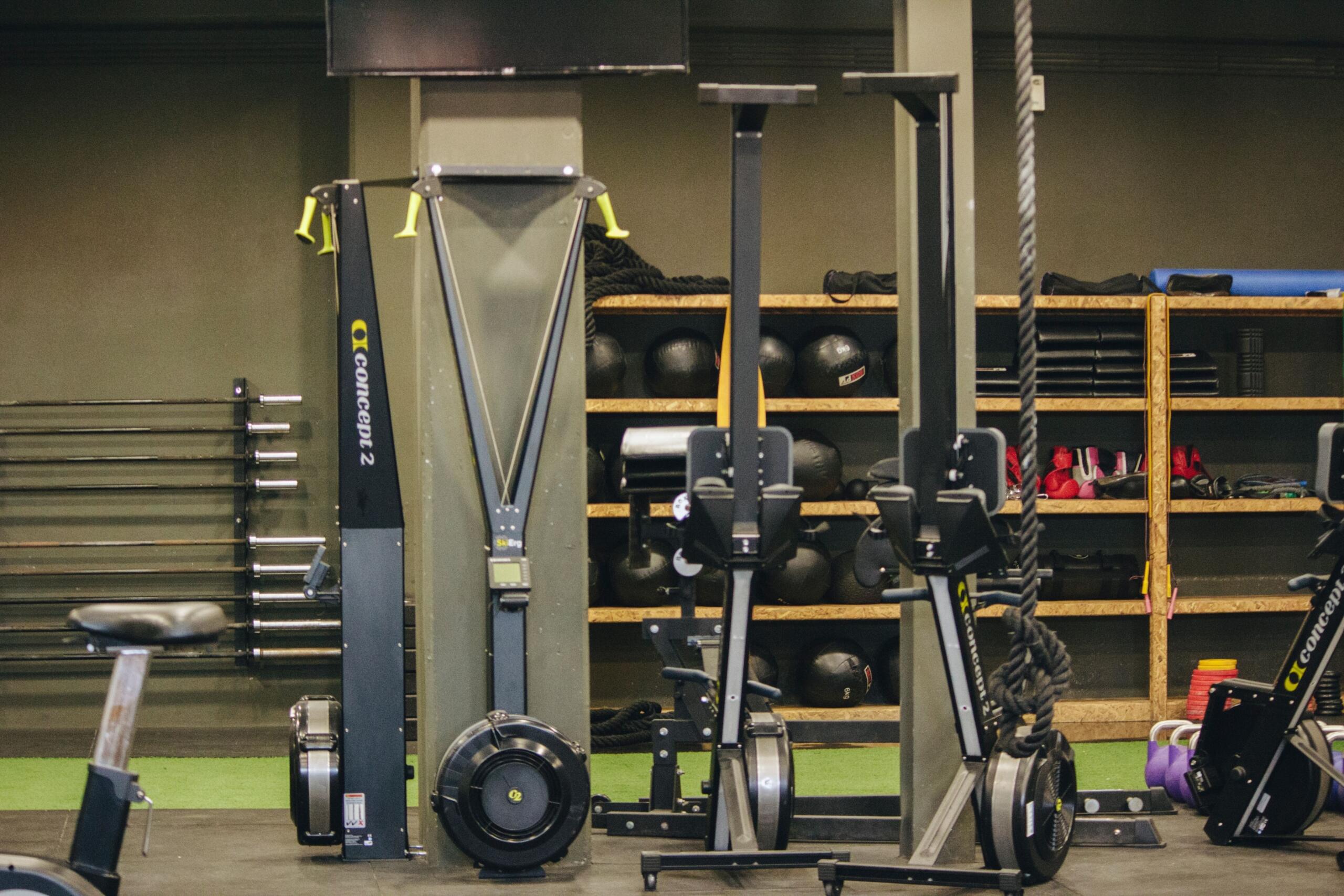 Several erg machines are lined up in a modern gym, ready for rowing and cardio training as part of a functional fitness workout.