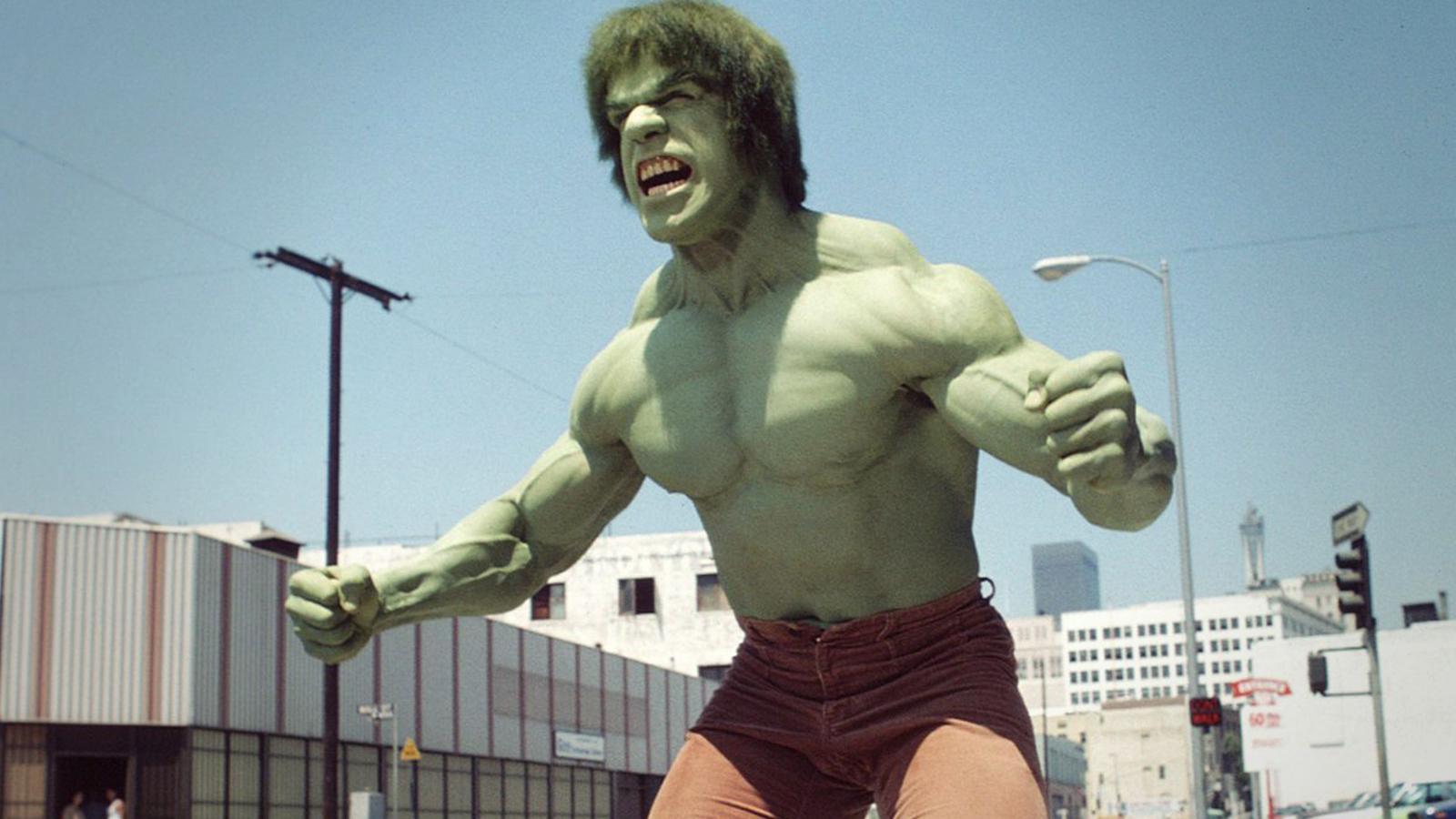 A muscular, green character stands flexing and ready for action on an urban street, with buildings and power lines in the background.
