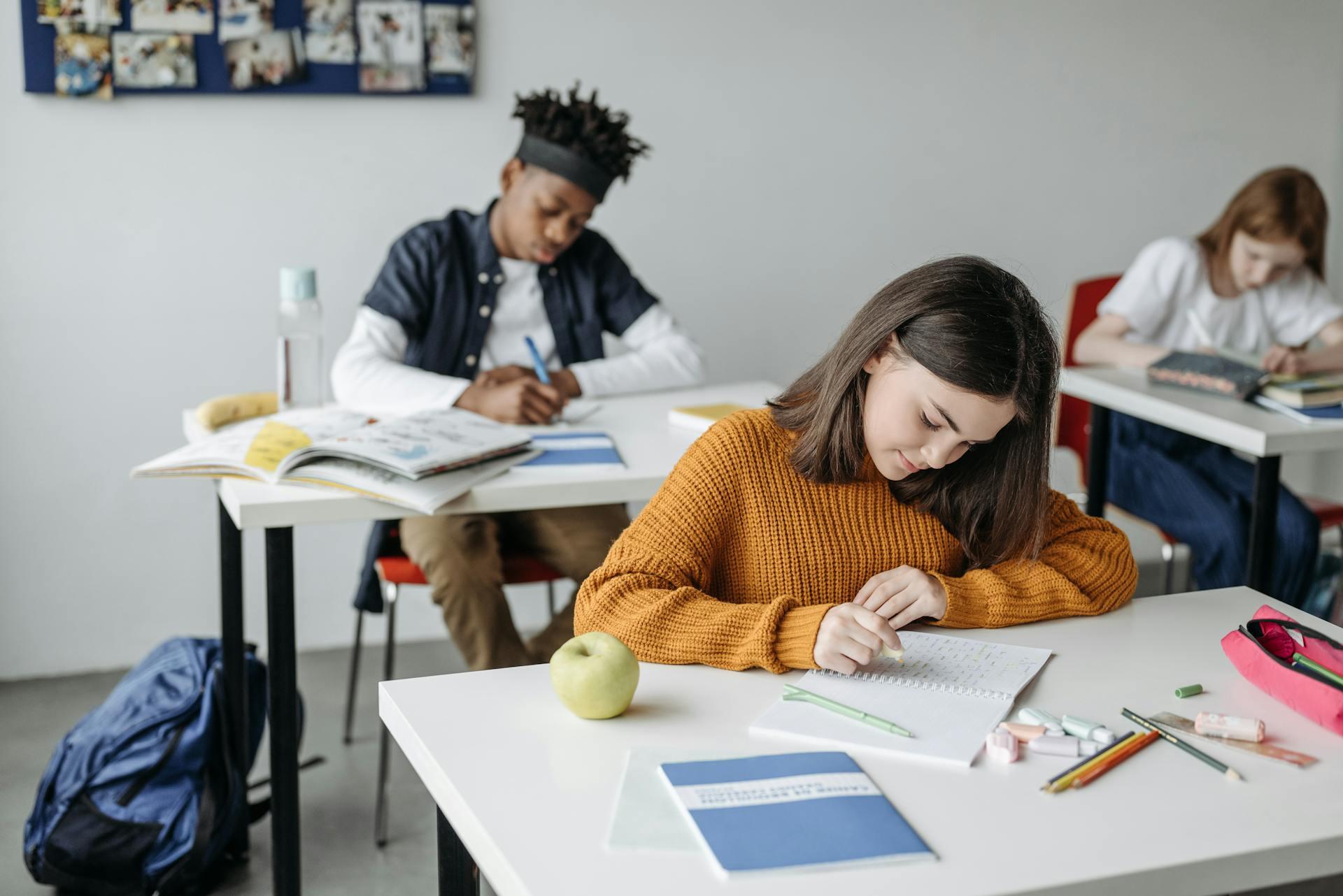 Three students sitting at their desks in a classroom during school, concentrating.
