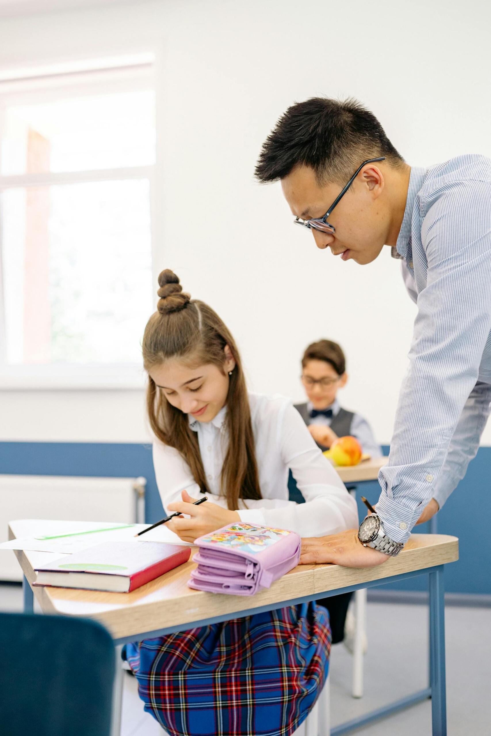 A private tutor teaching a high school girl to do her homework while she is sitting in a classroom.