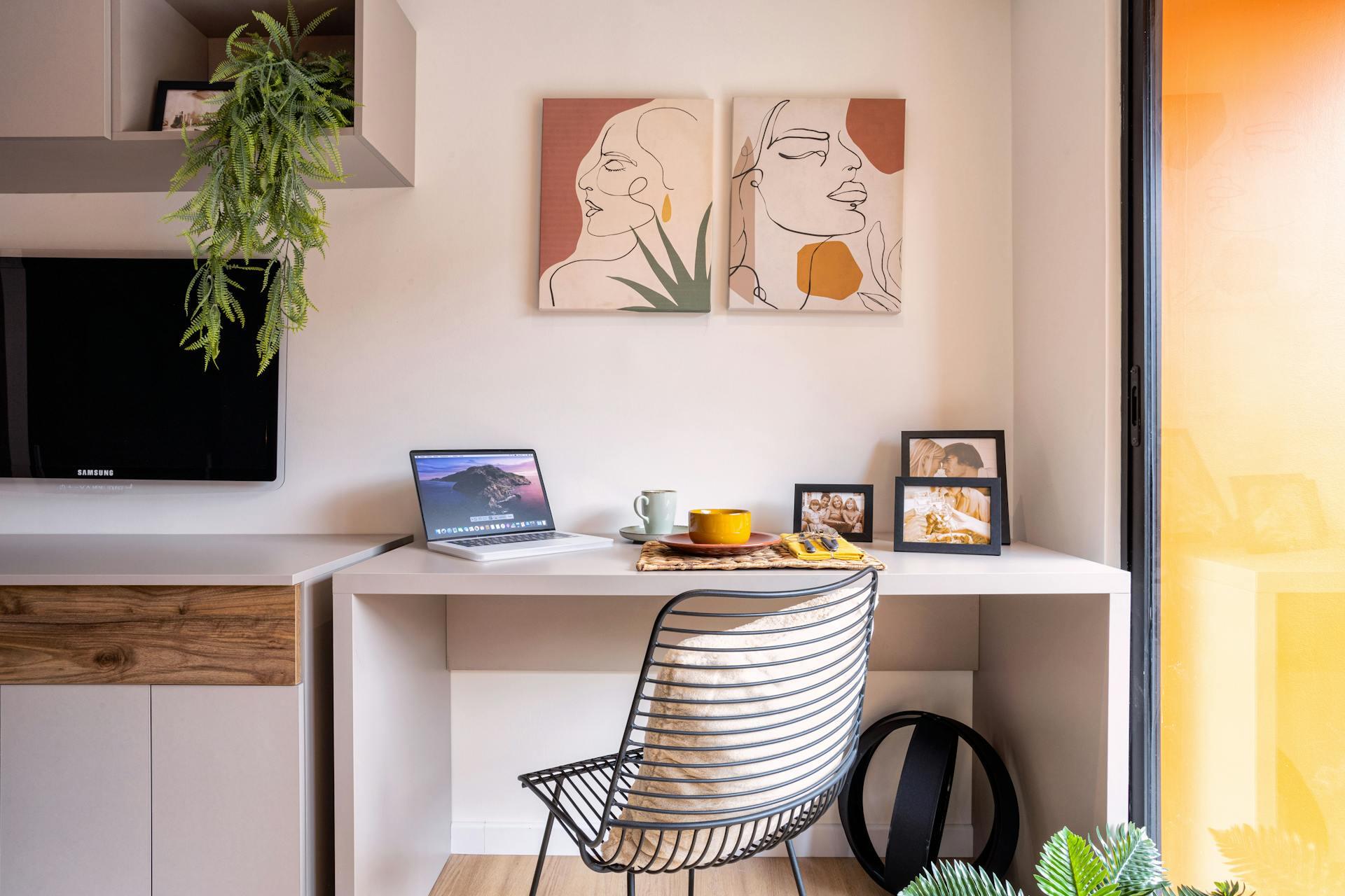 A modern workspace with a sleek desk, laptop, decorative plant, framed photos, and two abstract portraits on the wall.