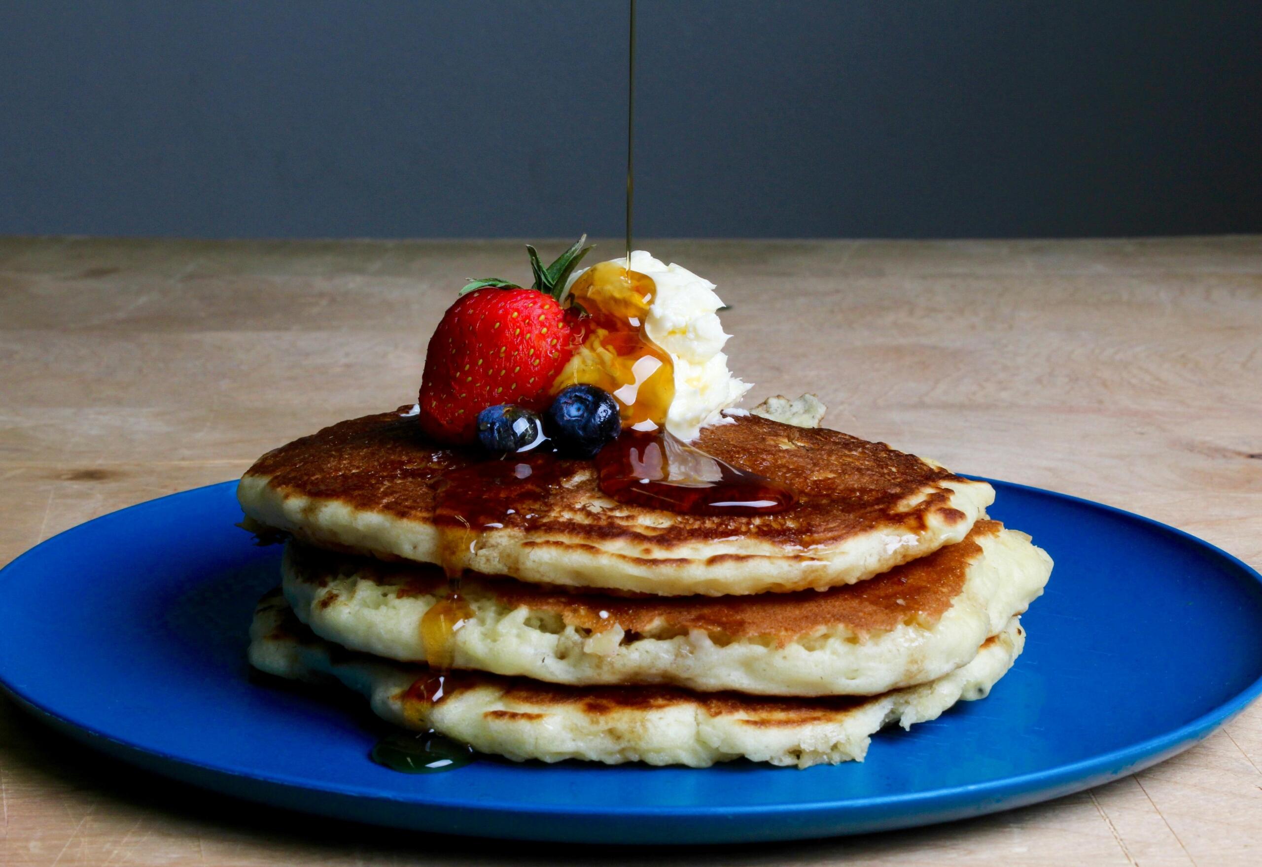A blue plate has a stack of three pancakes topped with a strawberry, two blueberries, and butter.