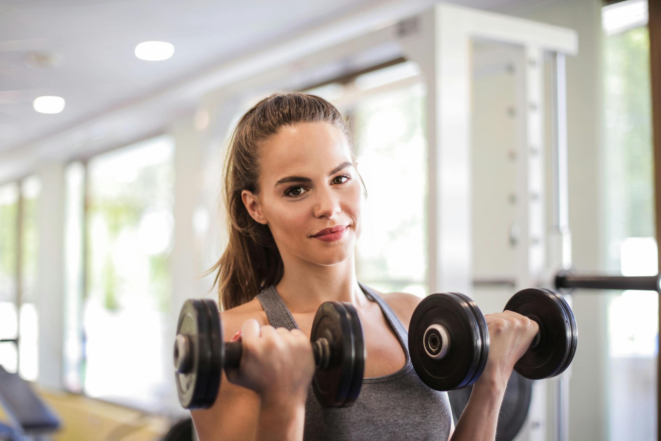 A girl holding 2 dumbbells up to her face. 