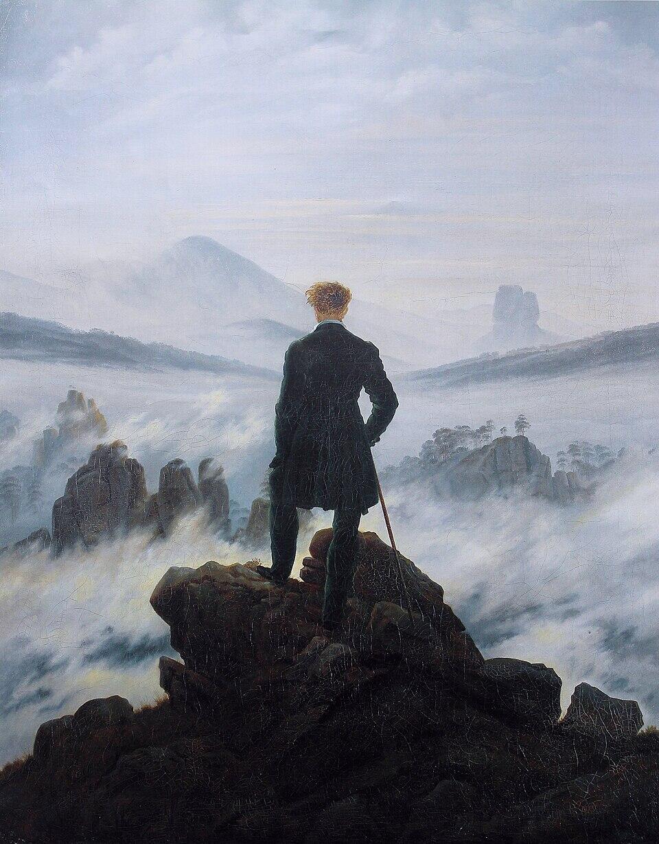 A man in dark clothing stands on a rocky cliff, overlooking a misty mountainous landscape under a cloudy sky.