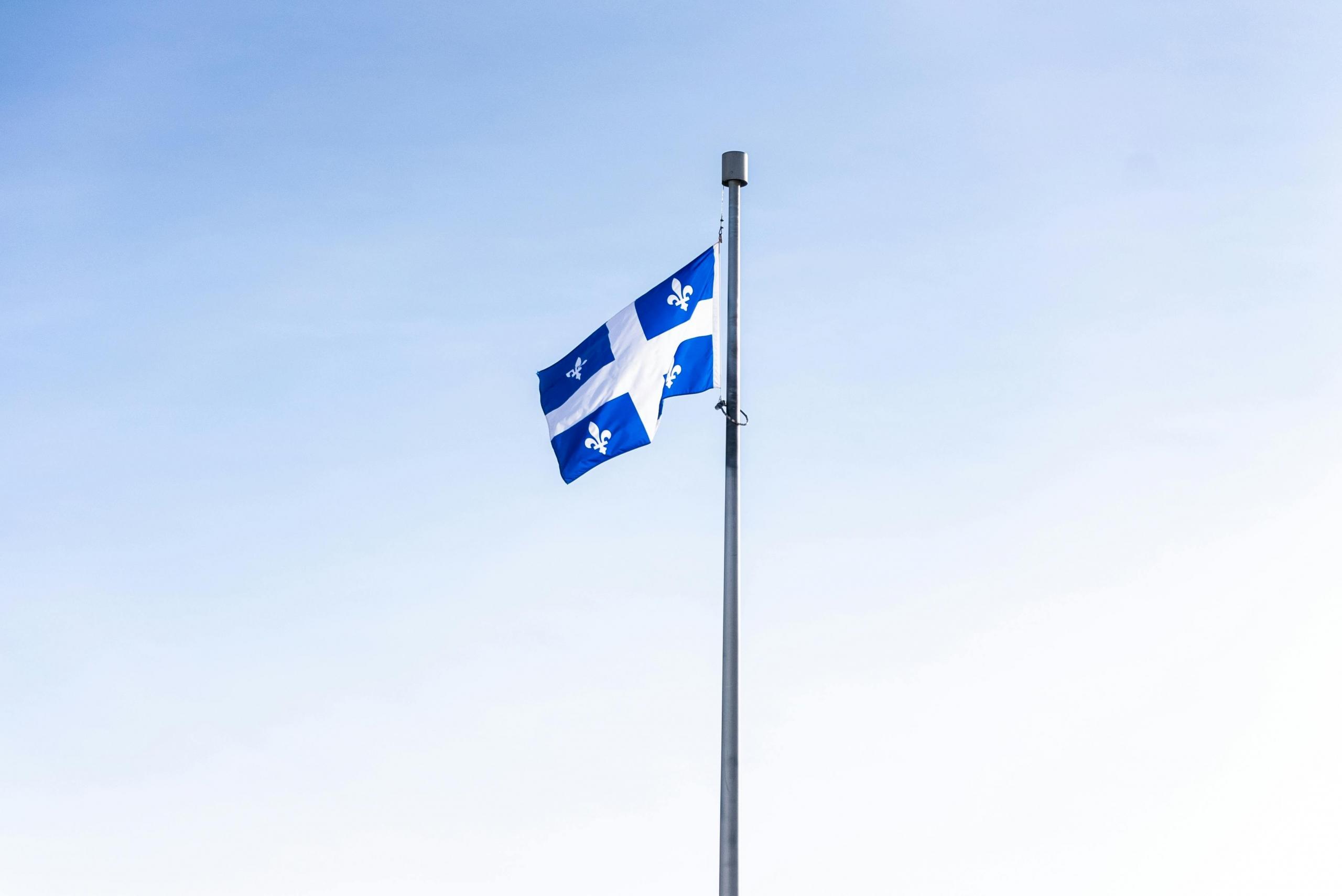 The flag of Quebec flies. The sky in the background is blue.