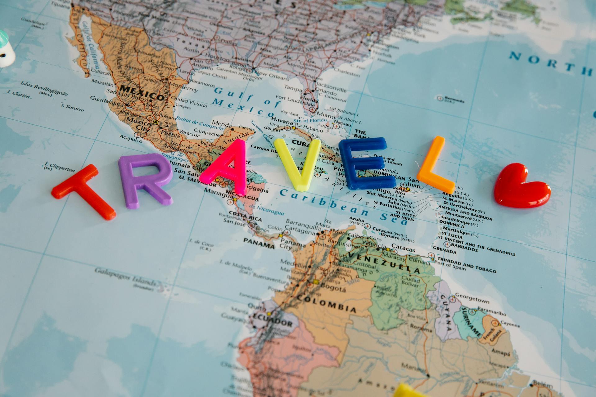 Colorful plastic letters spelling "TRAVEL" and a heart sit on a map of Central America and the Caribbean, symbolizing adventure.
