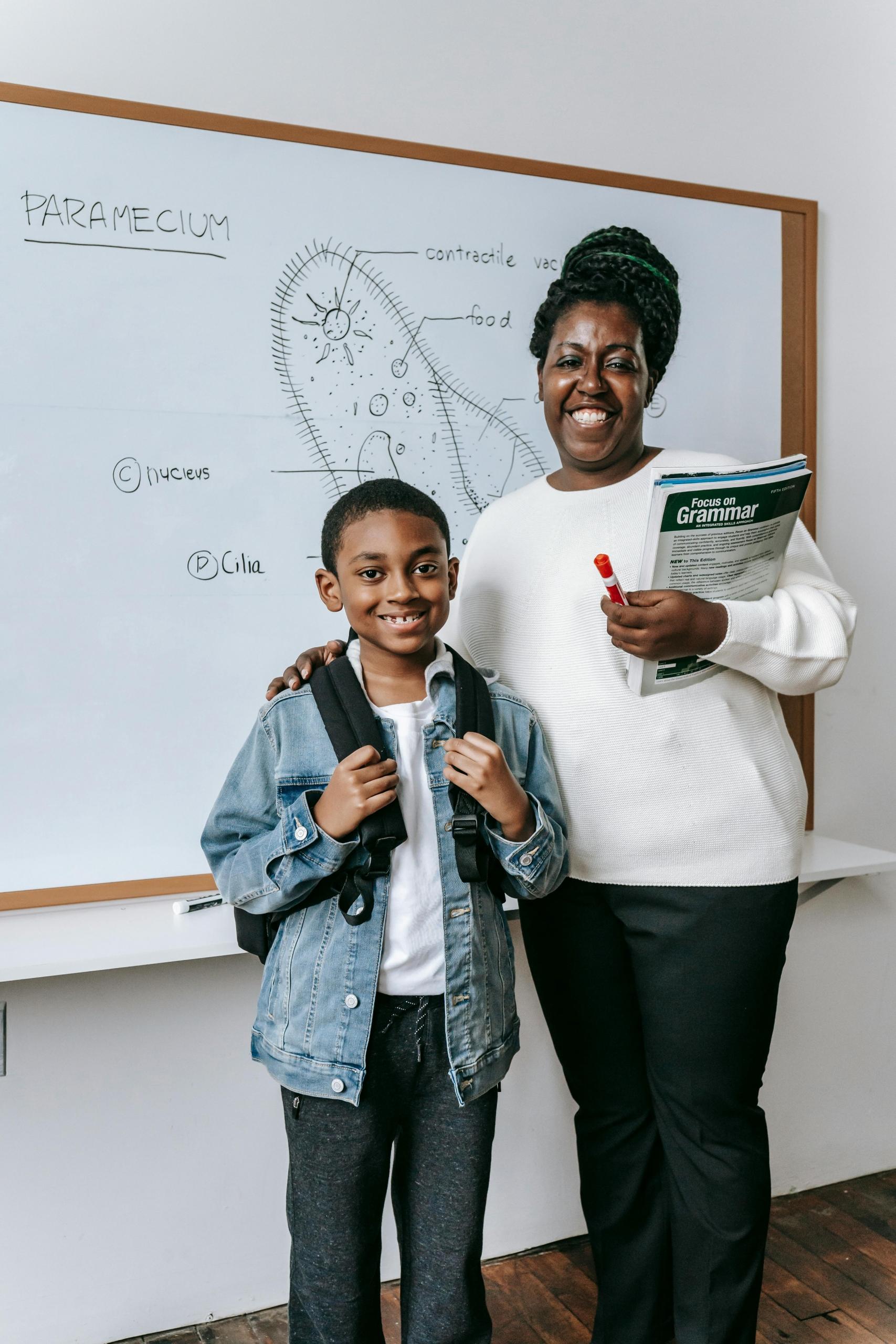a teacher stands with an elementary aged student in front of a white board. The white board has a diagram of a cell.