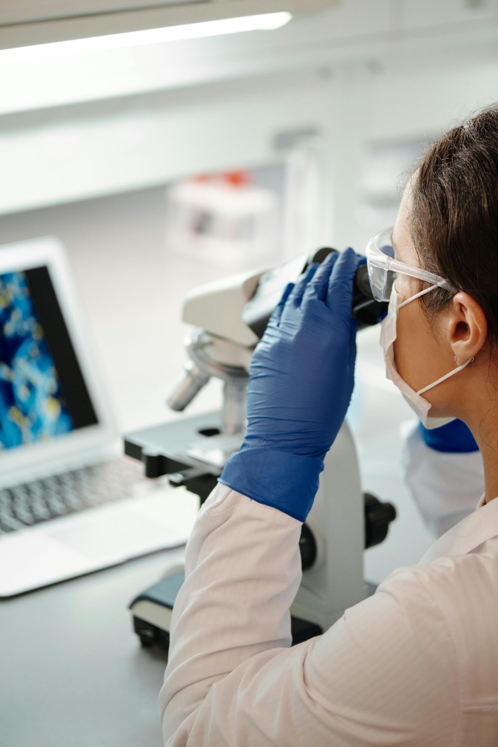 Woman in a lab coat looking into a microscope, conducting a scientific experiment in a laboratory setting.