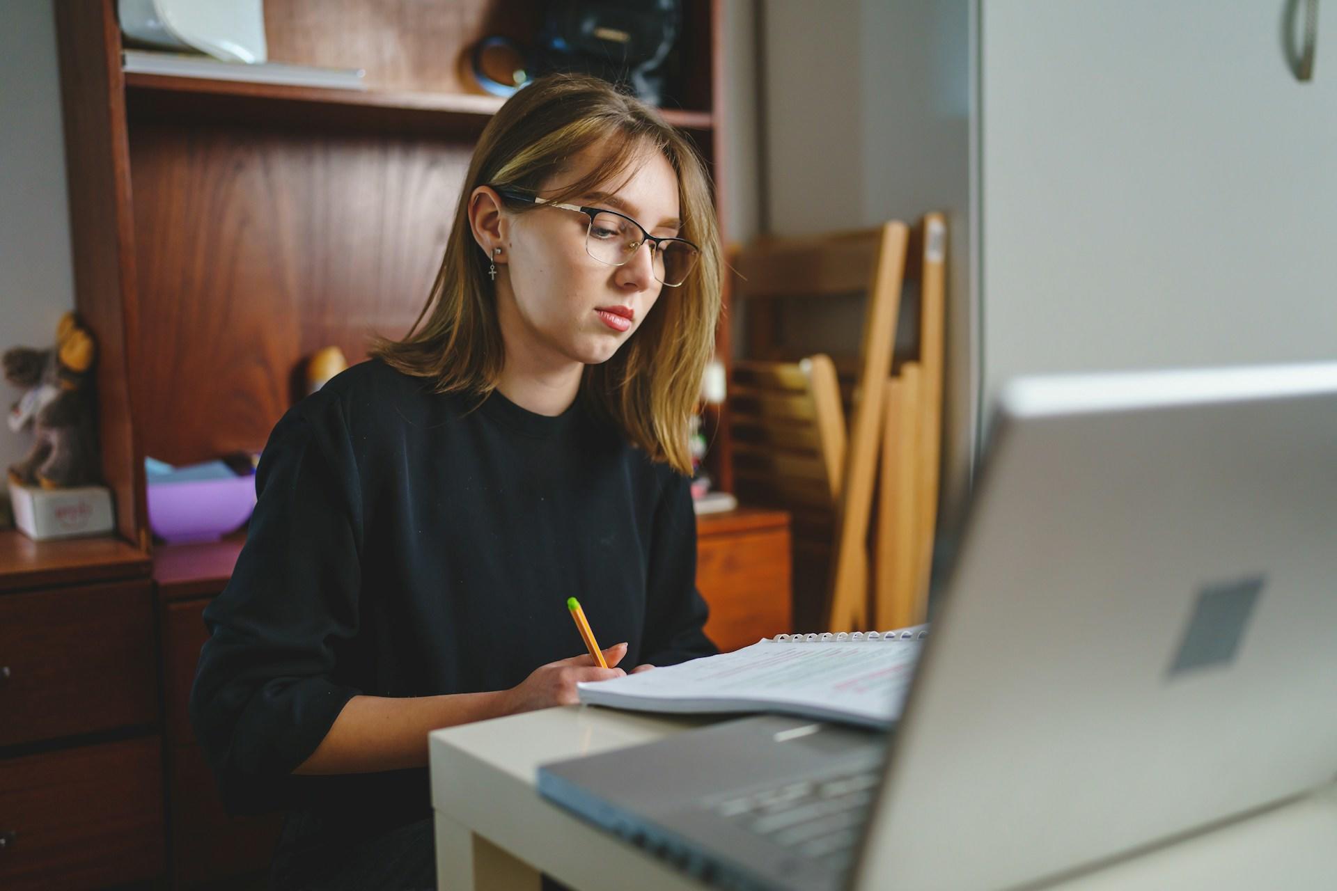 A girl sitting a desk with her laptop looking at stats work.
