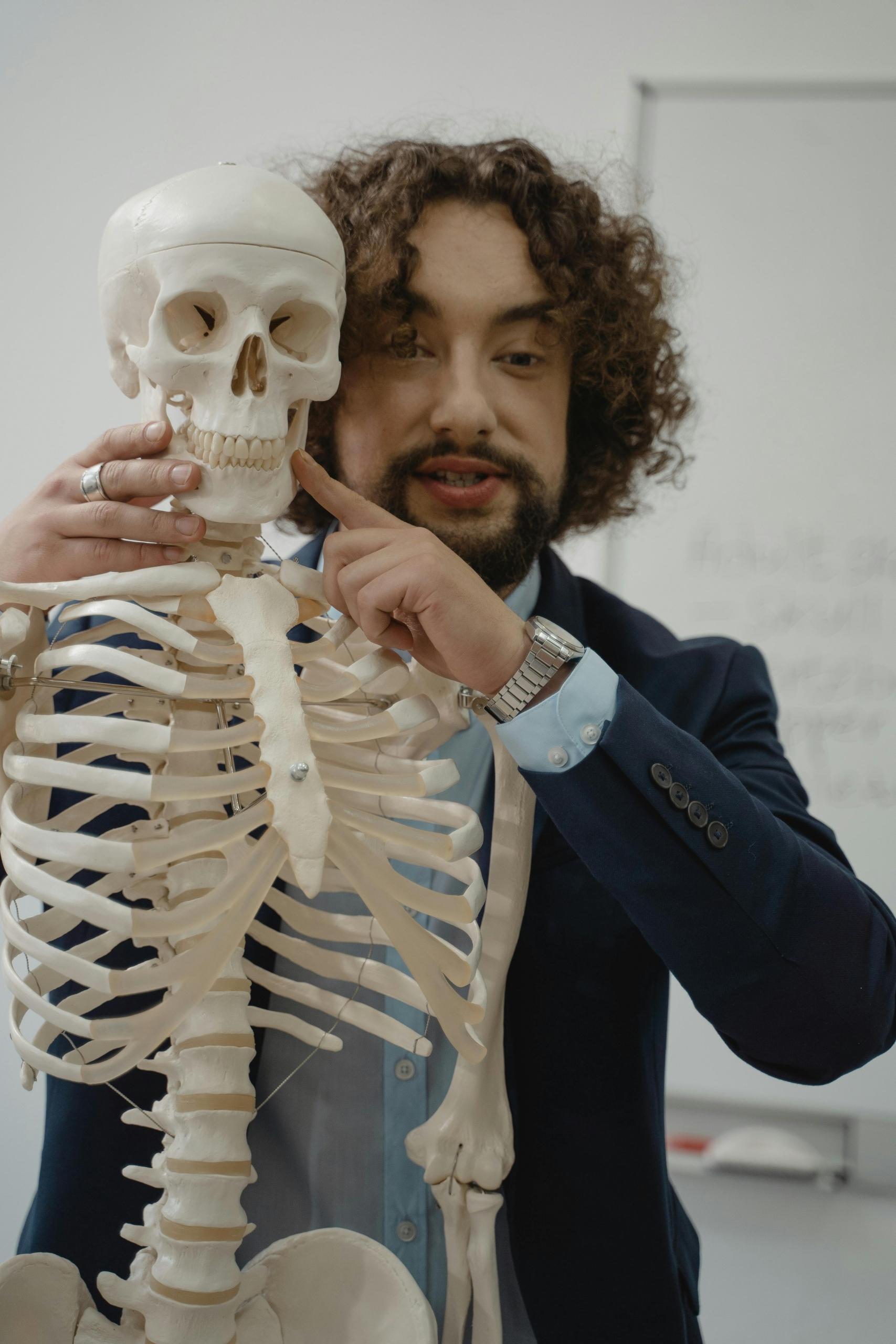 A biology teacher holding a skeleton demonstrating anatomy. 