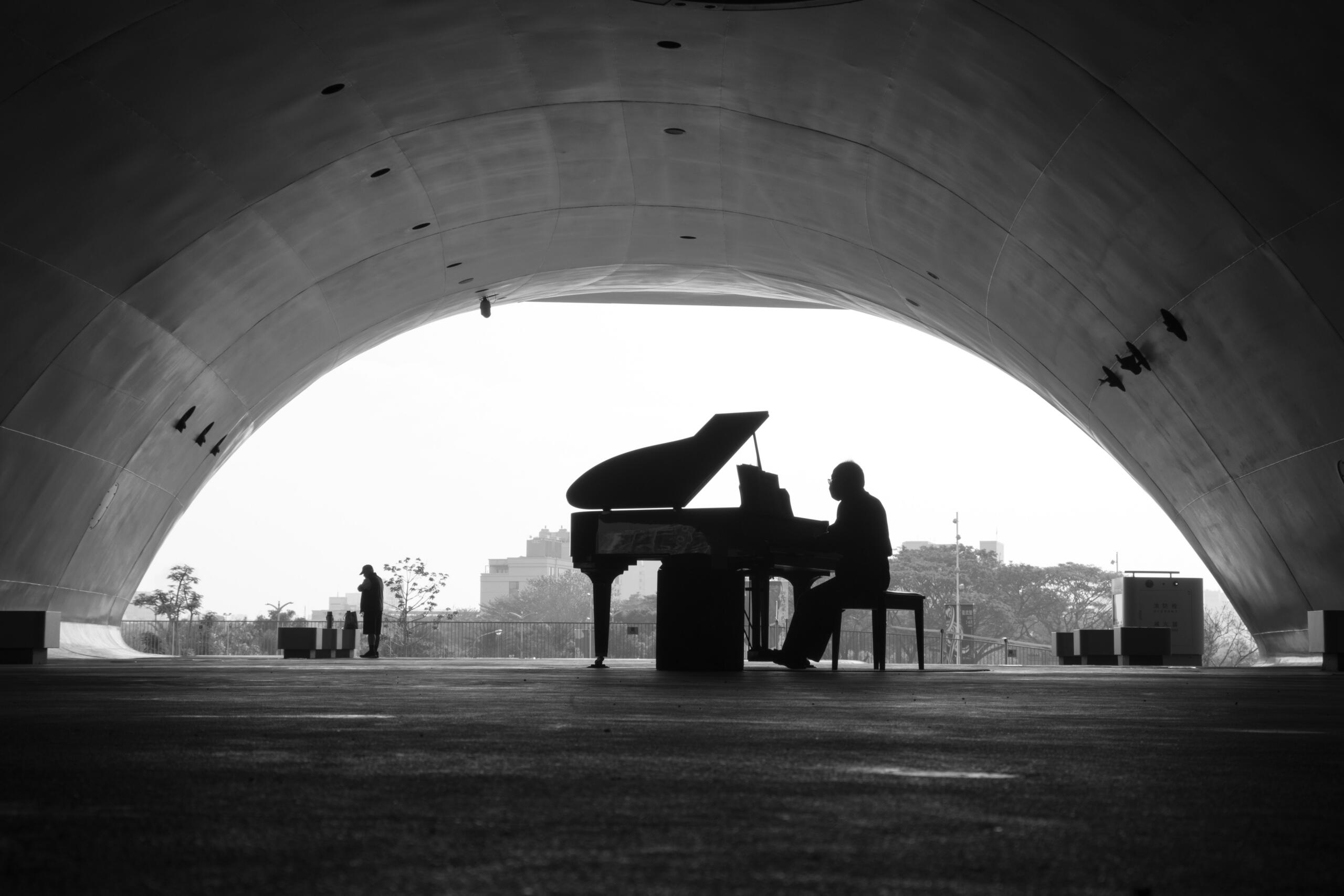 A silhouette of a pianist performing under a large archway, with a distant figure and urban scenery in monochrome tones.