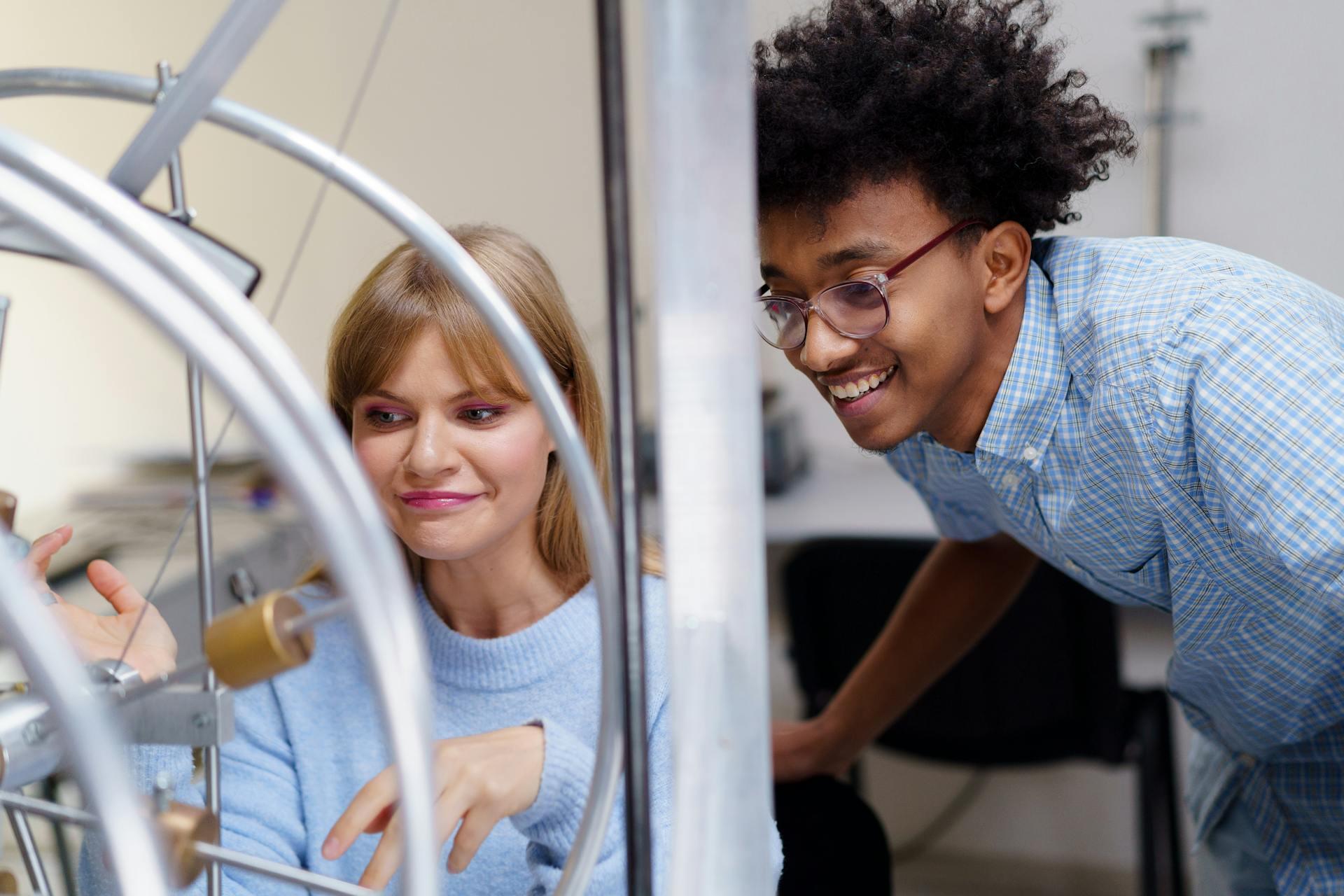A person gestures animatedly while discussing ideas with another person in a creative workspace, surrounded by equipment and tools.
