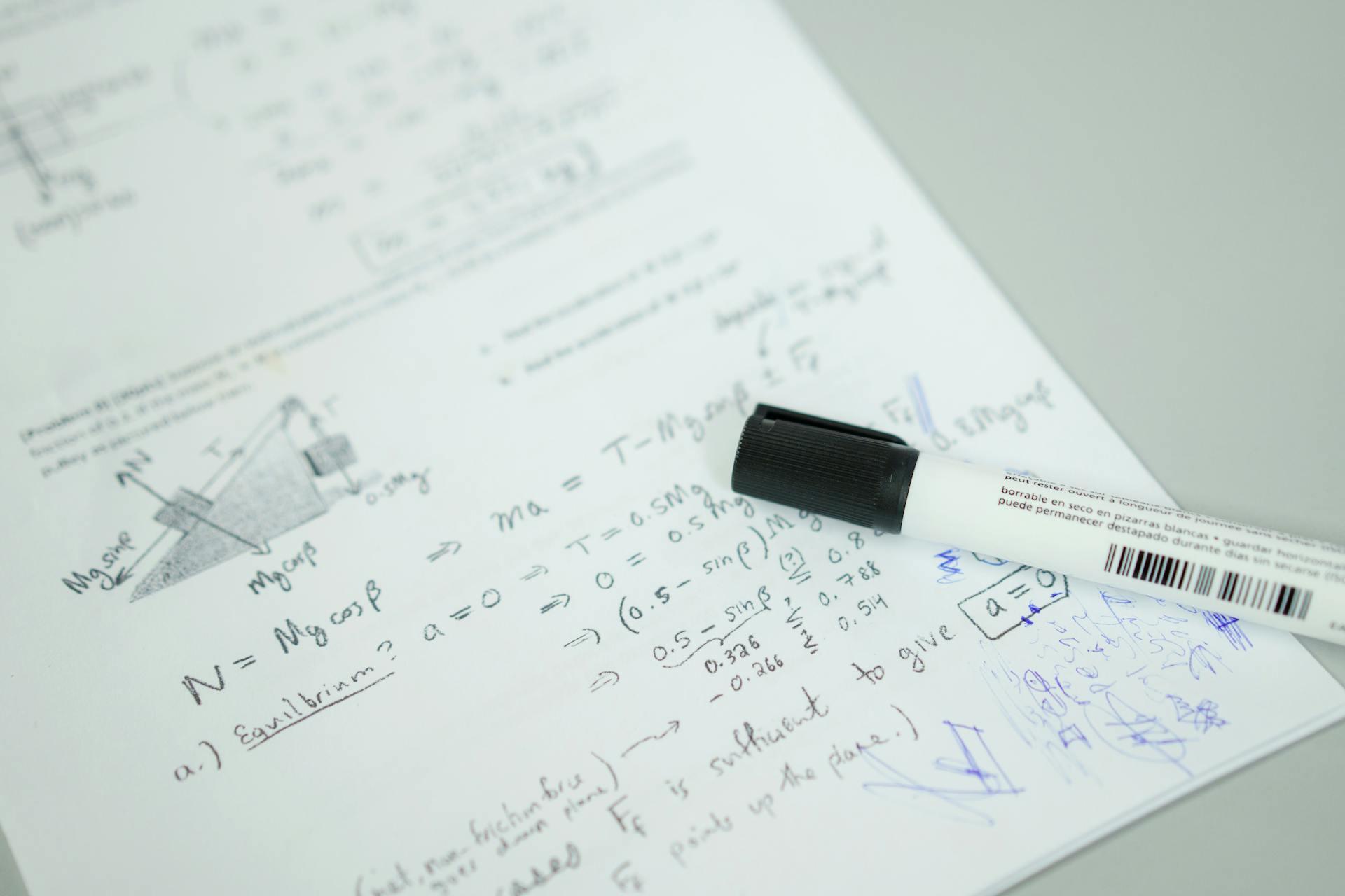 A close-up of handwritten physics equations and diagrams on paper, with a black marker lying on top, focused on equilibrium problem-solving.