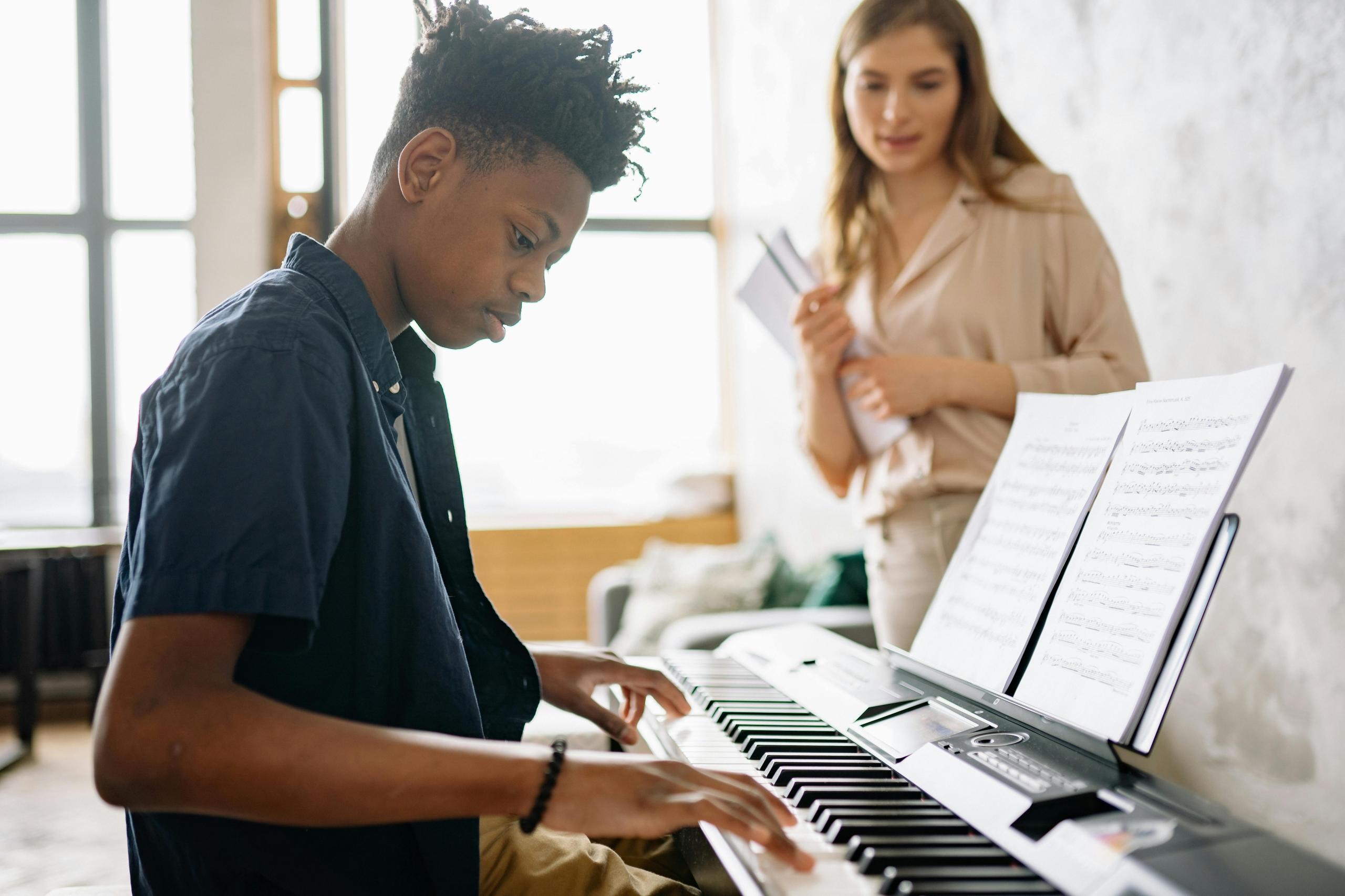 A piano teacher helping a student play the piano.