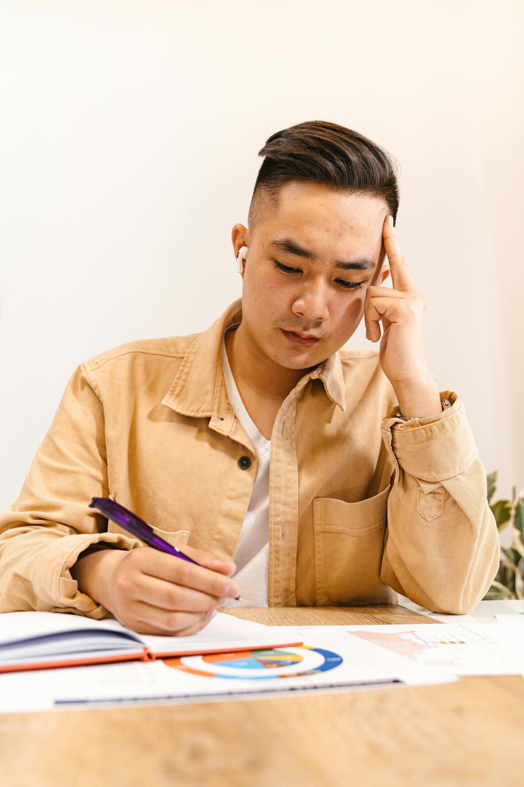 A teenage boy studies at a desk while examining graphs and charts on a computer screen or worksheet. He appears focused and engaged as he analyzes data, trends, and mathematical relationships, demonstrating critical thinking and problem-solving skills.