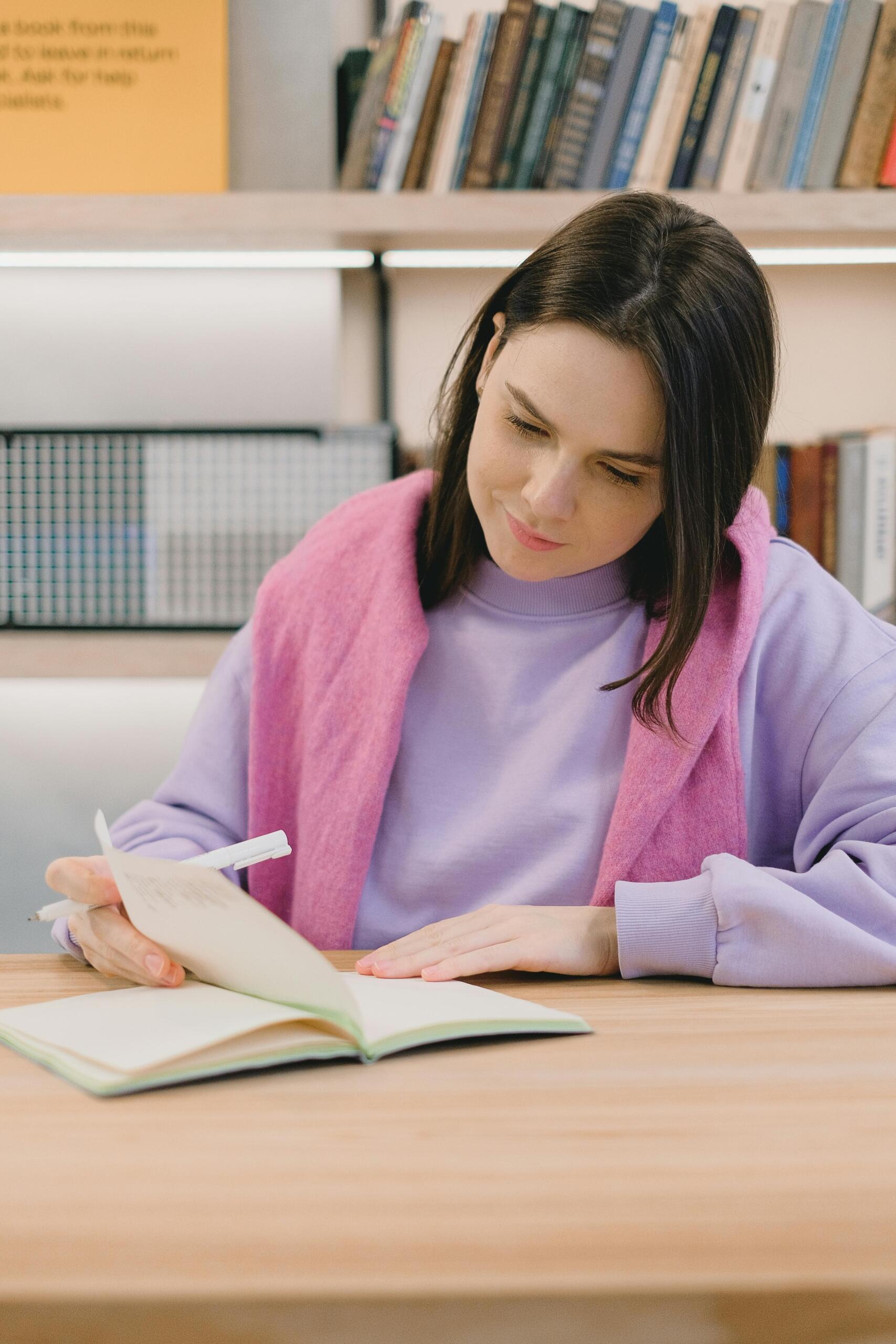 A girl sits quietly reading a book, concentrating on the pages in front of her. The image conveys learning, study, and academic engagement as she focuses on understanding the text.