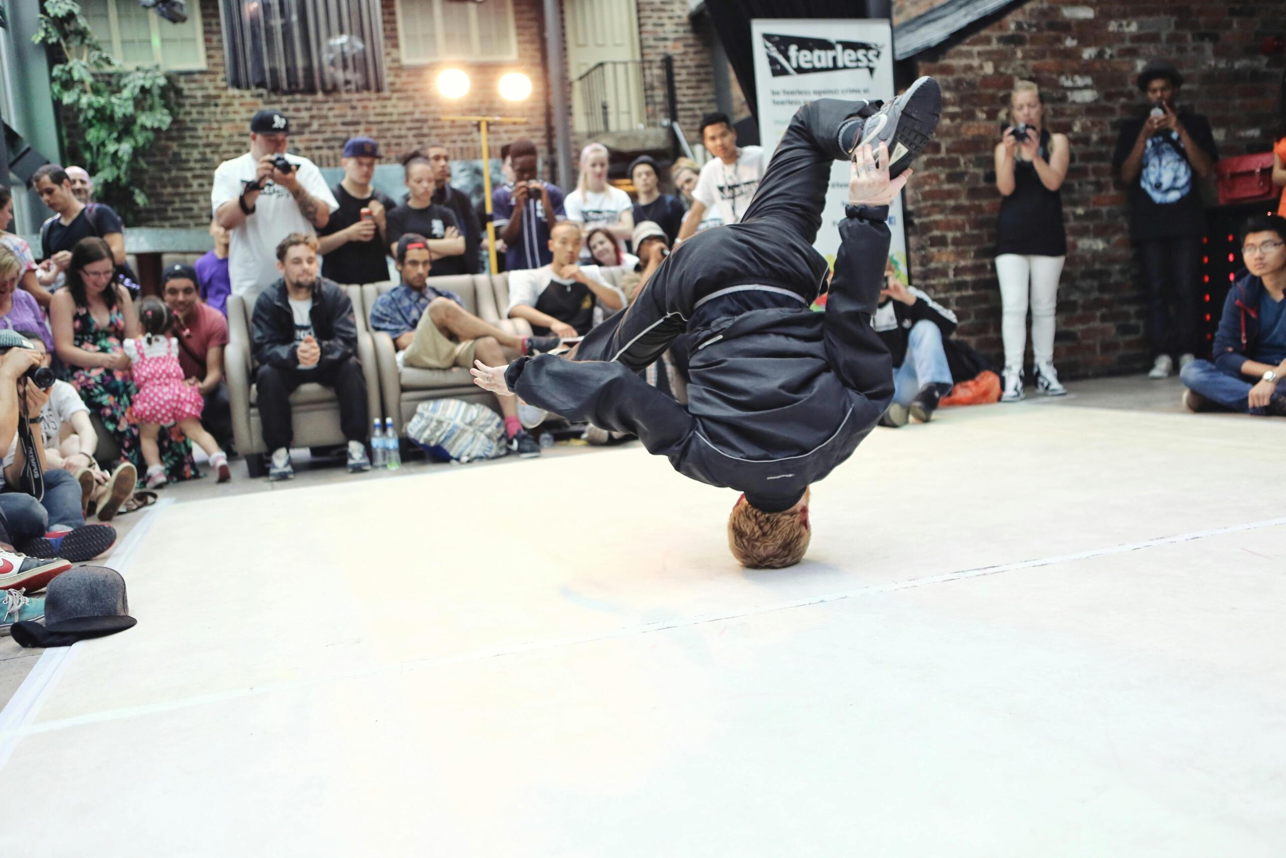 a man breakdances in front of a crowd. He is on a white stage.