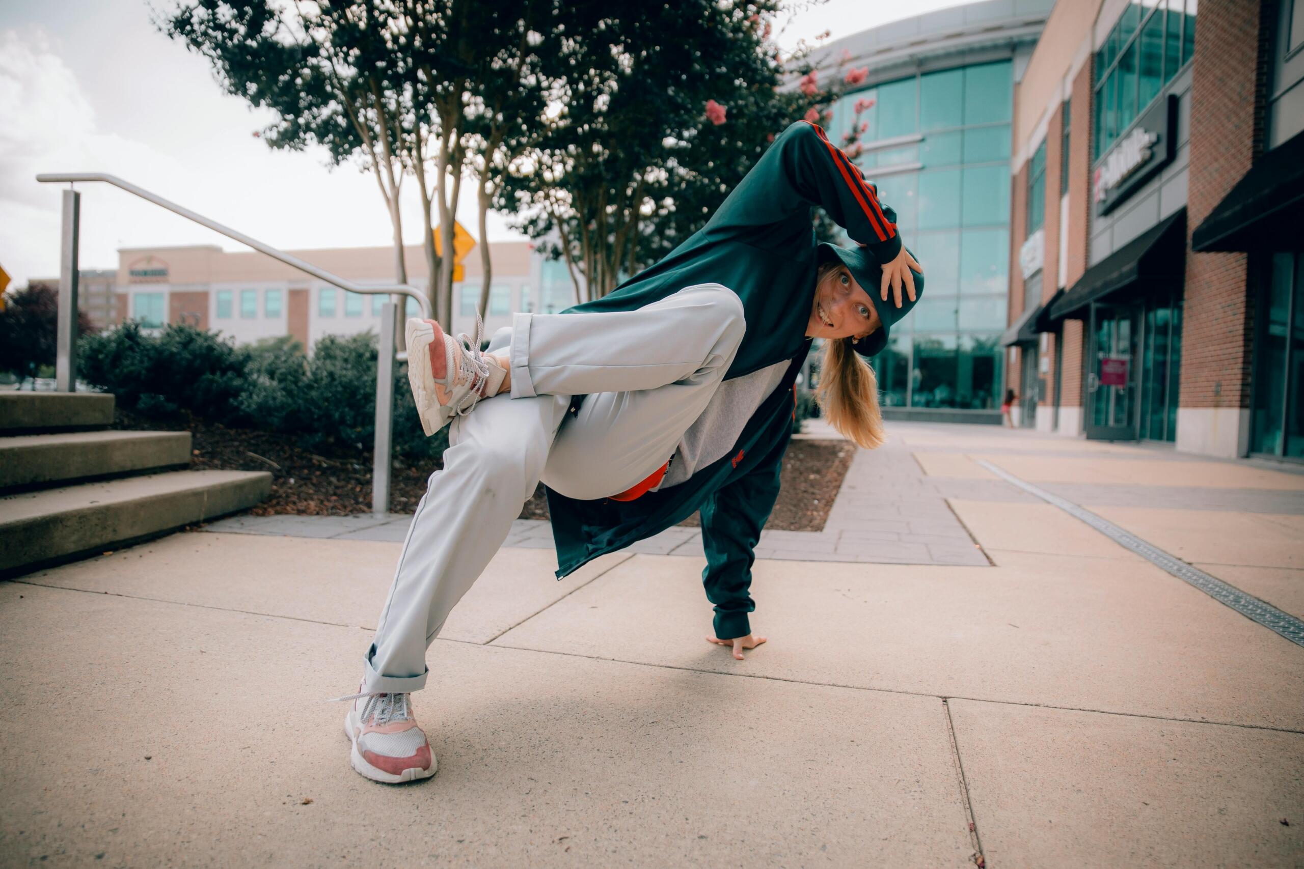 a young woman in casual clothing break dances in front of a shopping plaza.