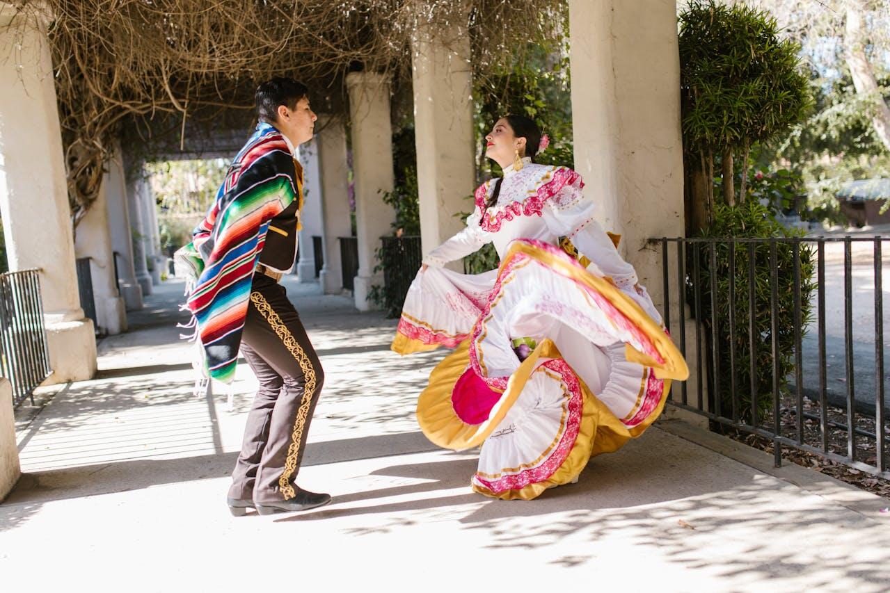 A couple performs a traditional dance in vibrant costumes, surrounded by elegant architecture and lush greenery.