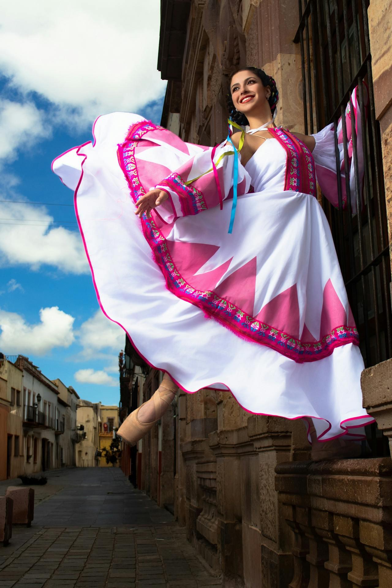 A dancer in a vibrant traditional dress twirls gracefully near a street lined with historic buildings under a blue sky.
