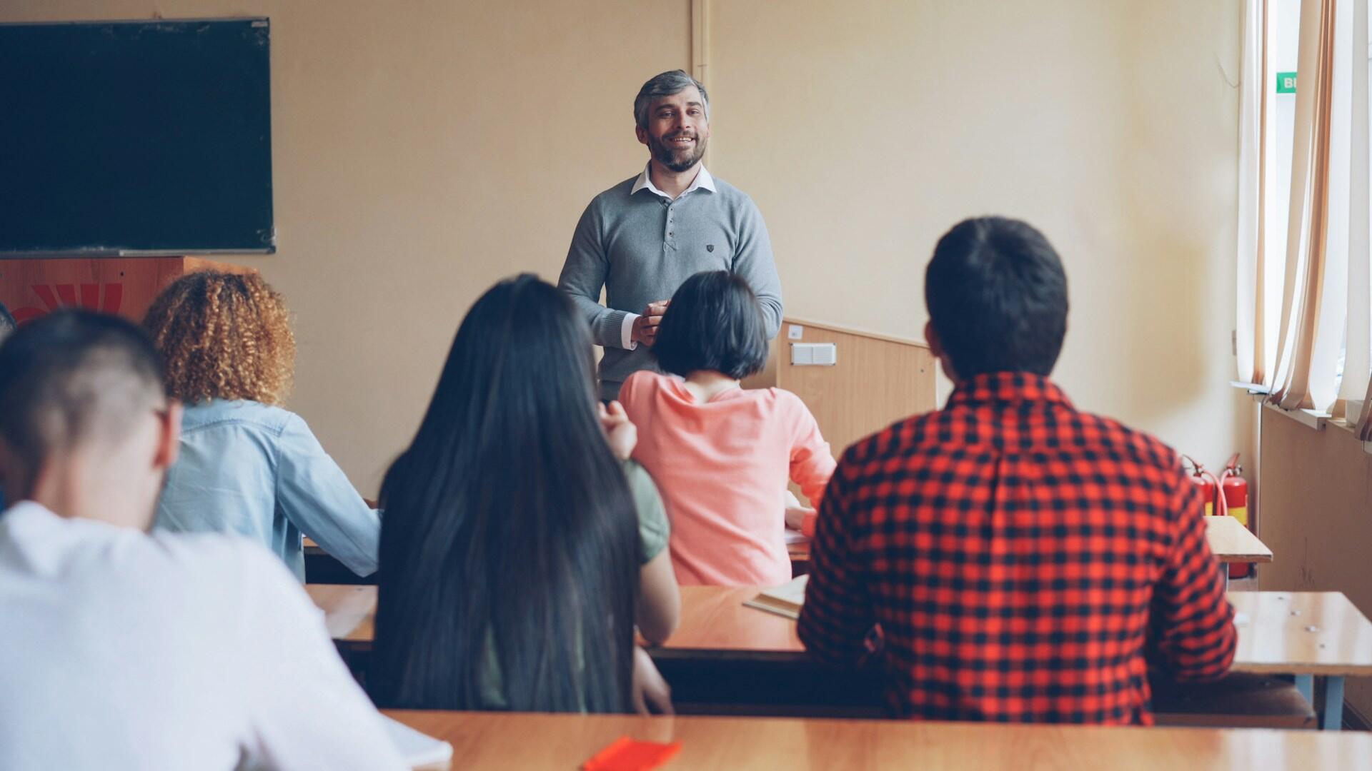 Teacher at the front of a classroom giving a lecture to a class of students