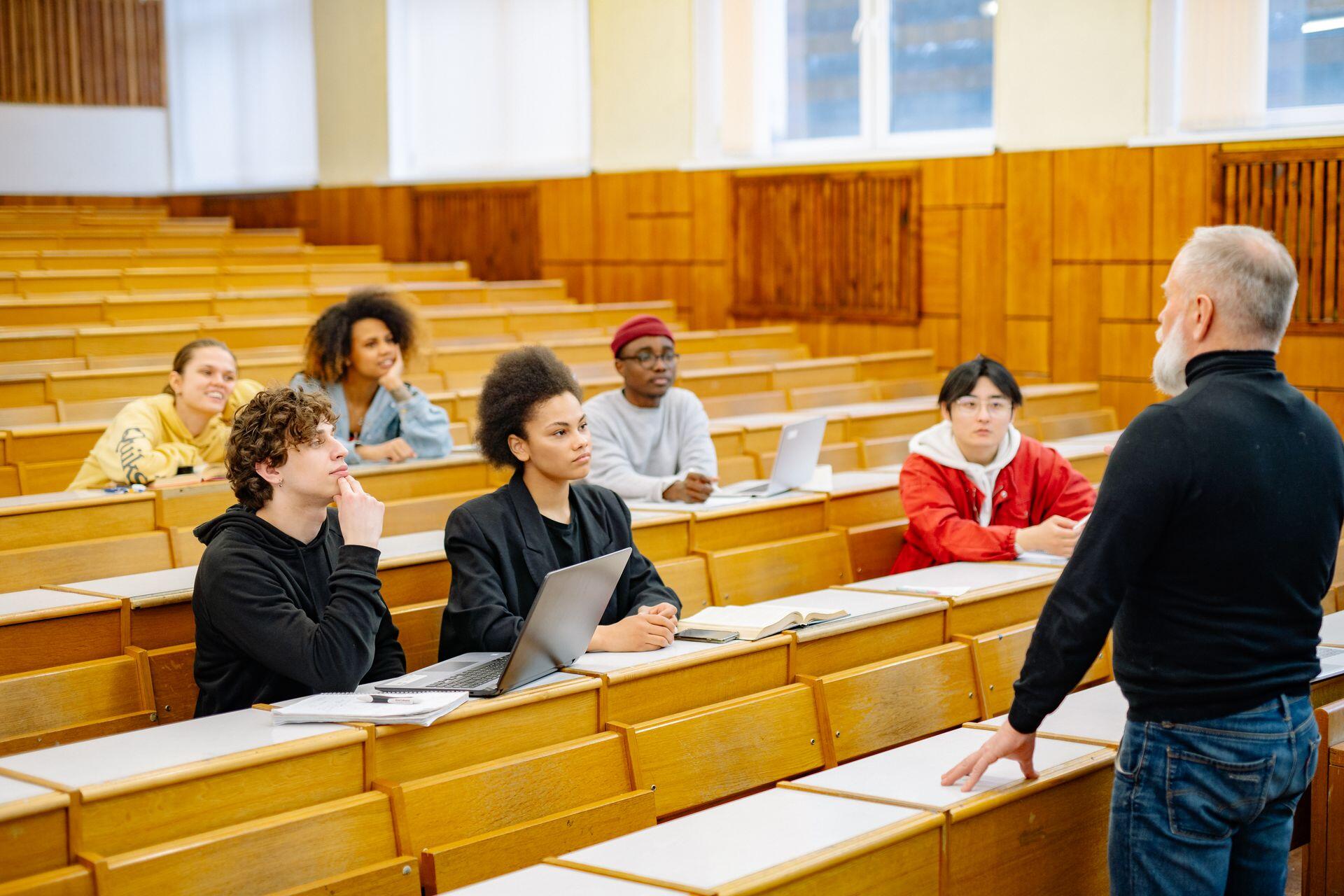 A professor stands at the front of a small class of students seated in a university lecture hall