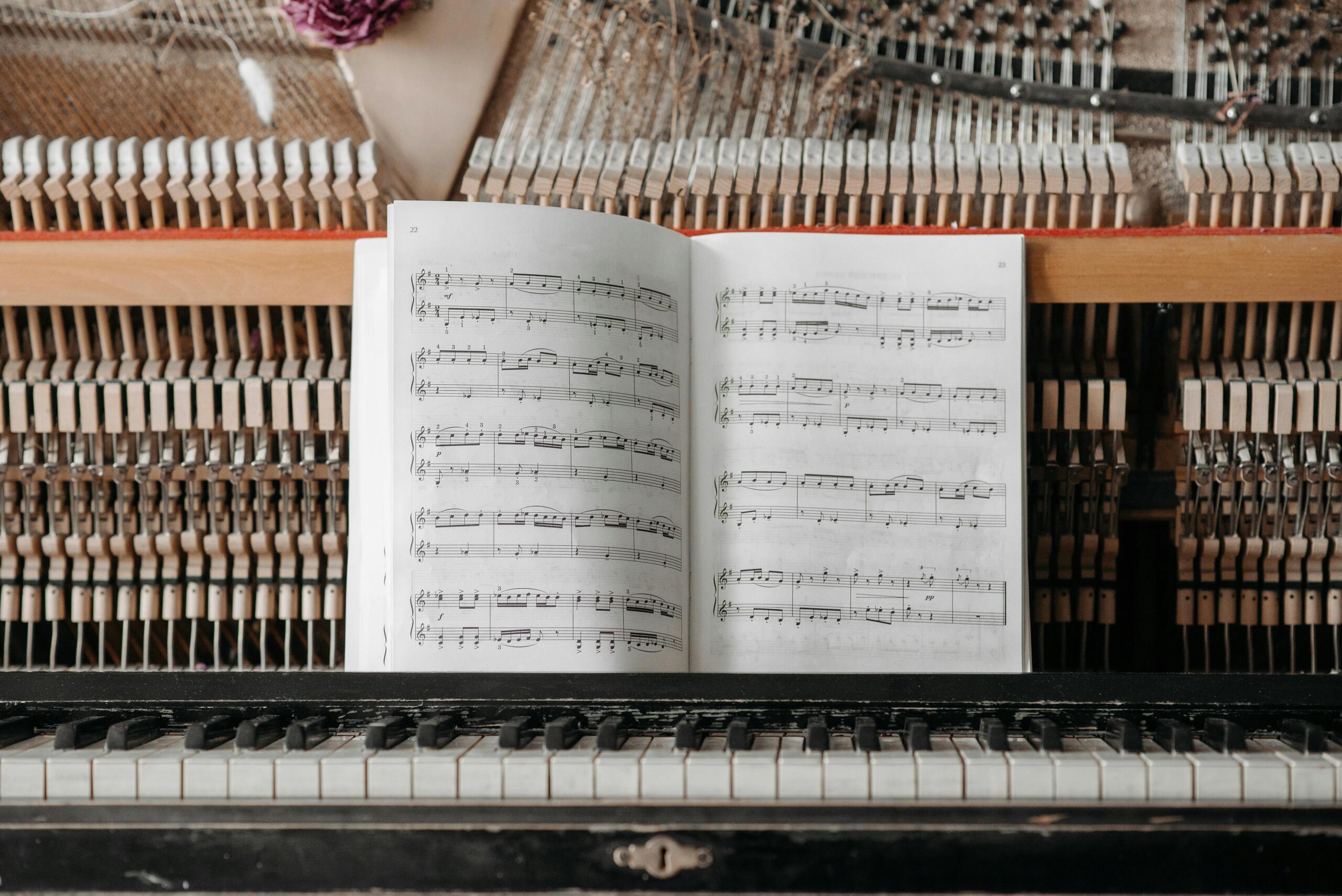 An open sheet music book displays notes above an old piano keyboard, with piano hammers visible in the background.