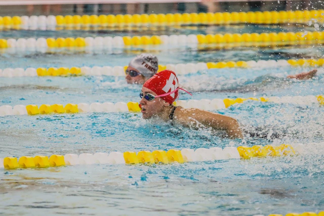 A swimmer doing laps in a lane pool with a red cap on.