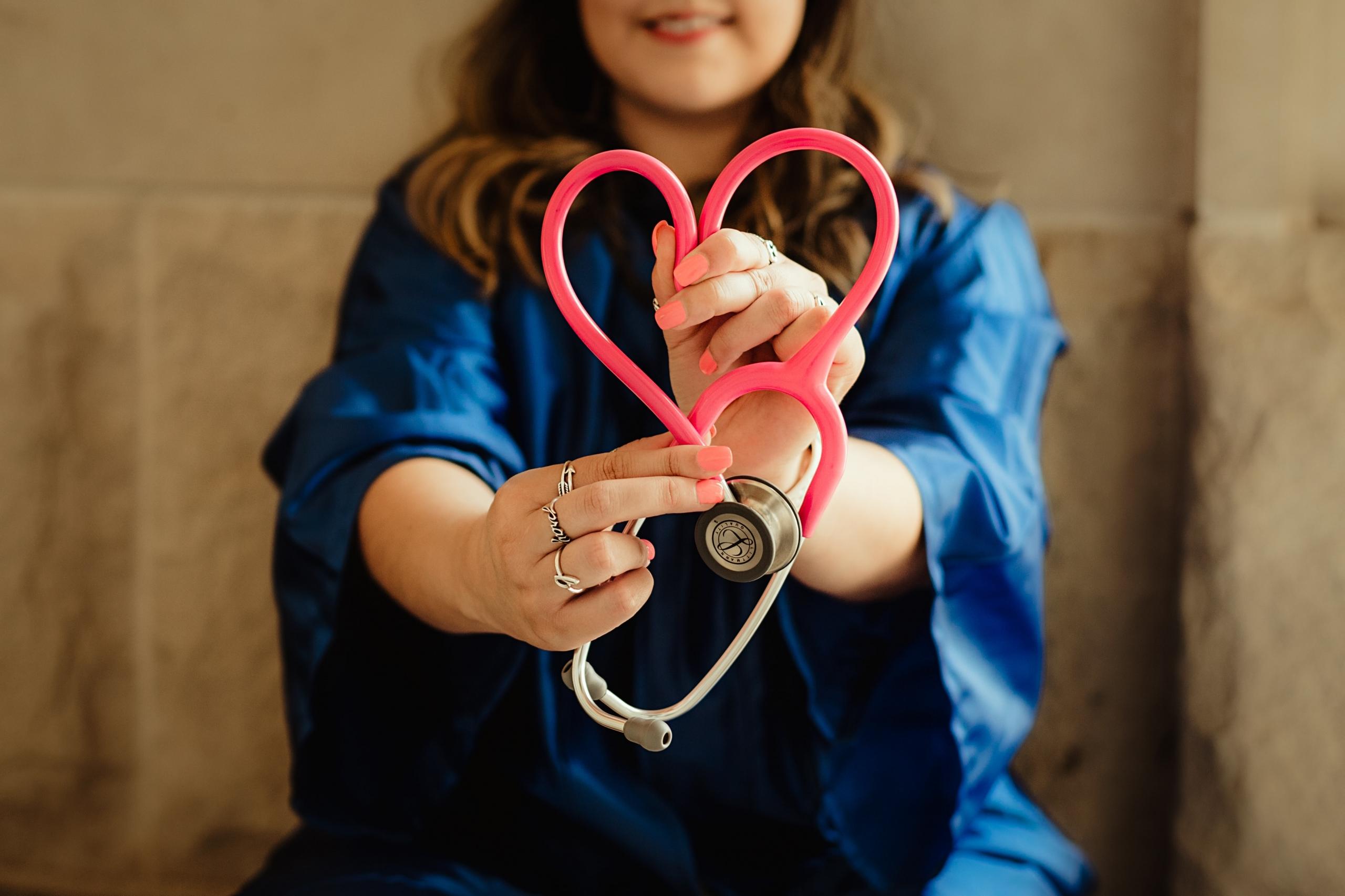 a nurse holds a stethoscope in the shape if a heart.