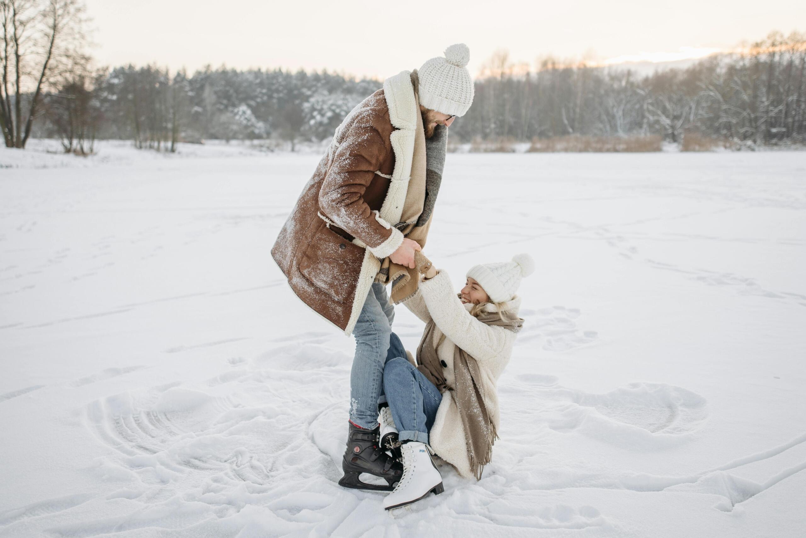 a man helps a woman get up while ice skating on a lake.
