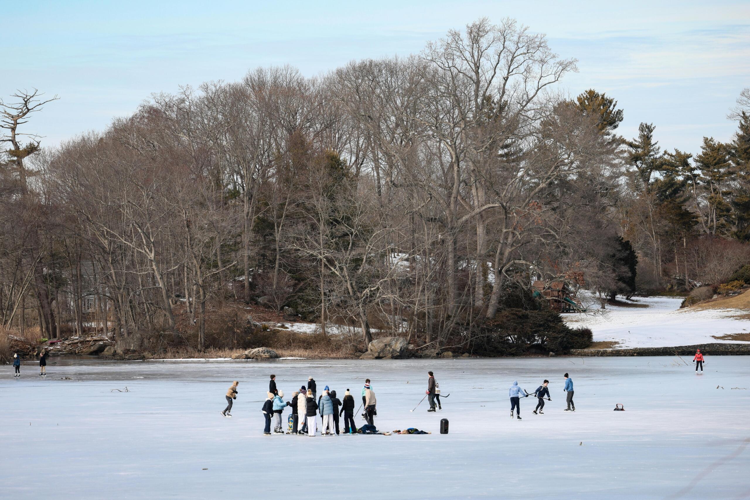 a group of people skate on a lake with a surrounding forest.