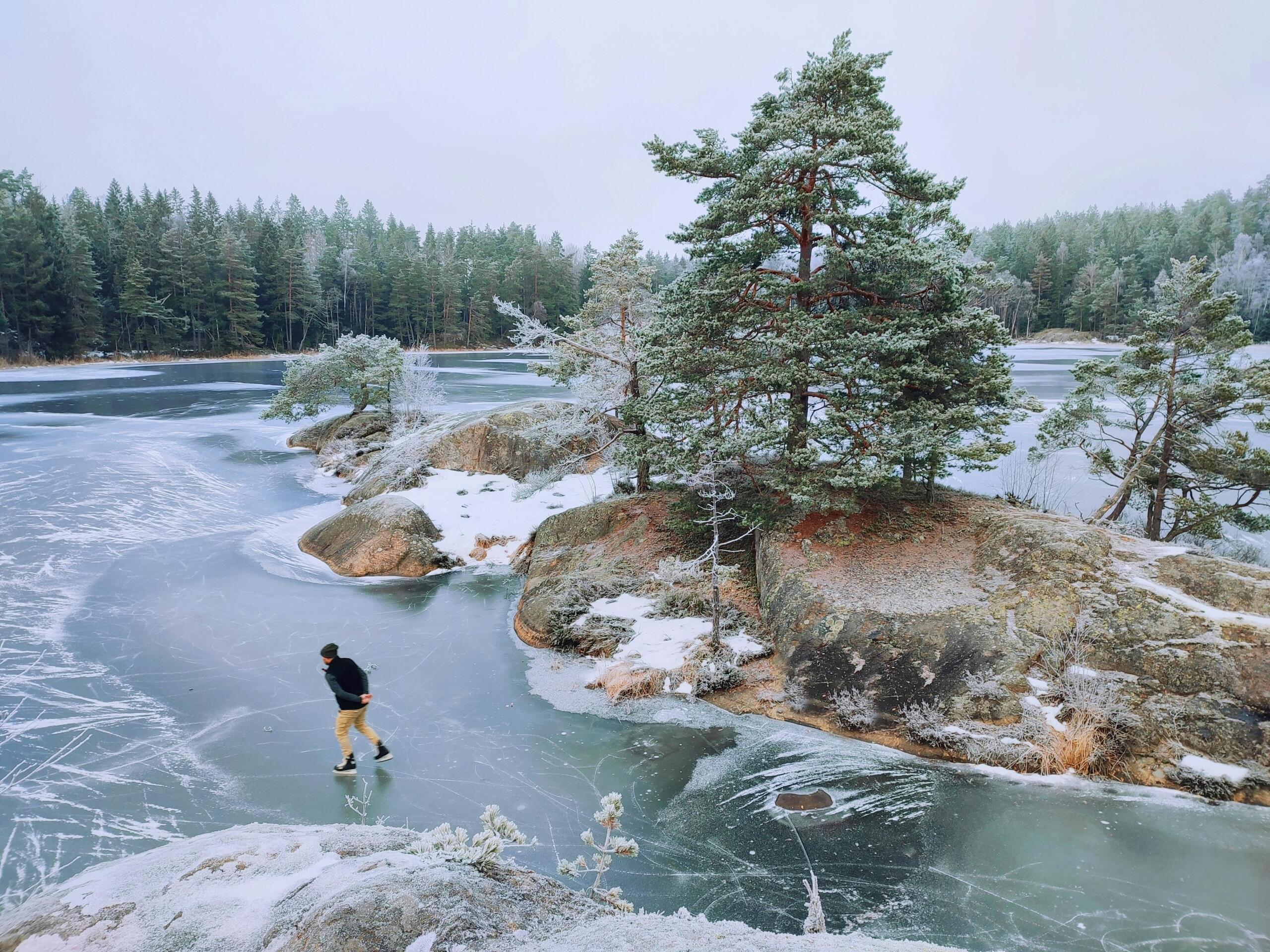 A man skates on a lake surrounded by forests.