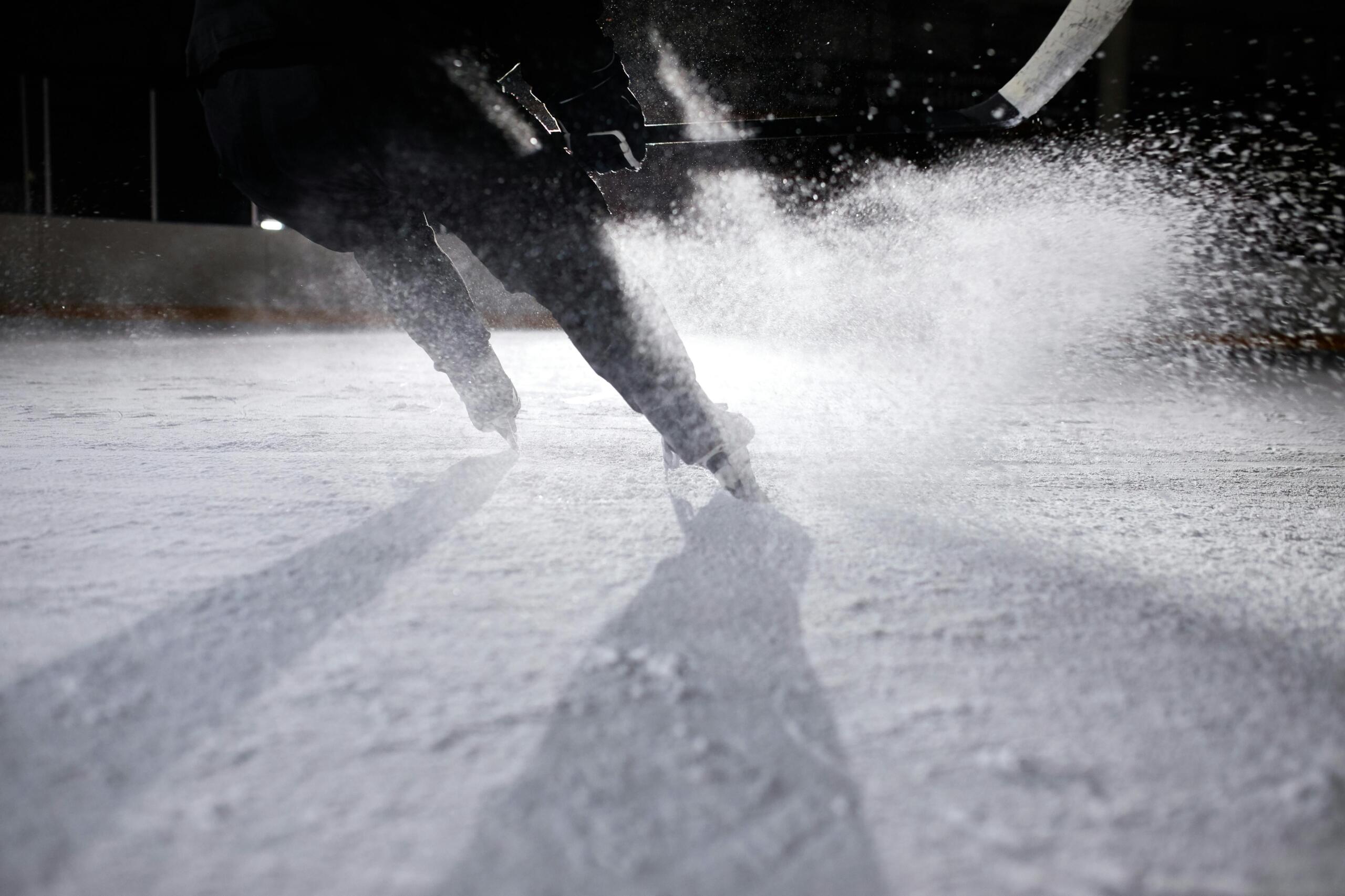 A hockey player moves quickly on the ice. Ice is spraying everywhere.