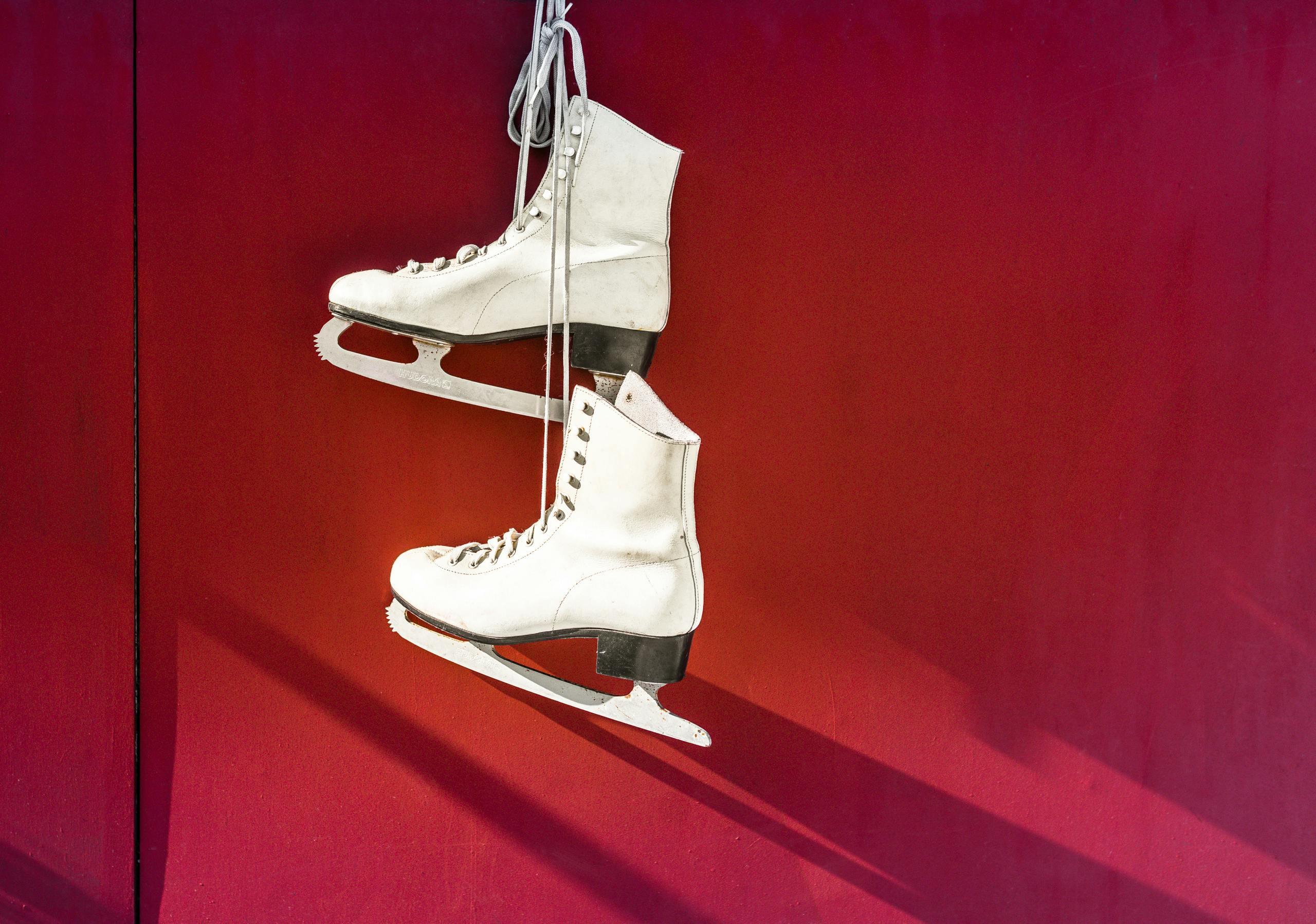 a pair of figure skates hangs in front of a red background.