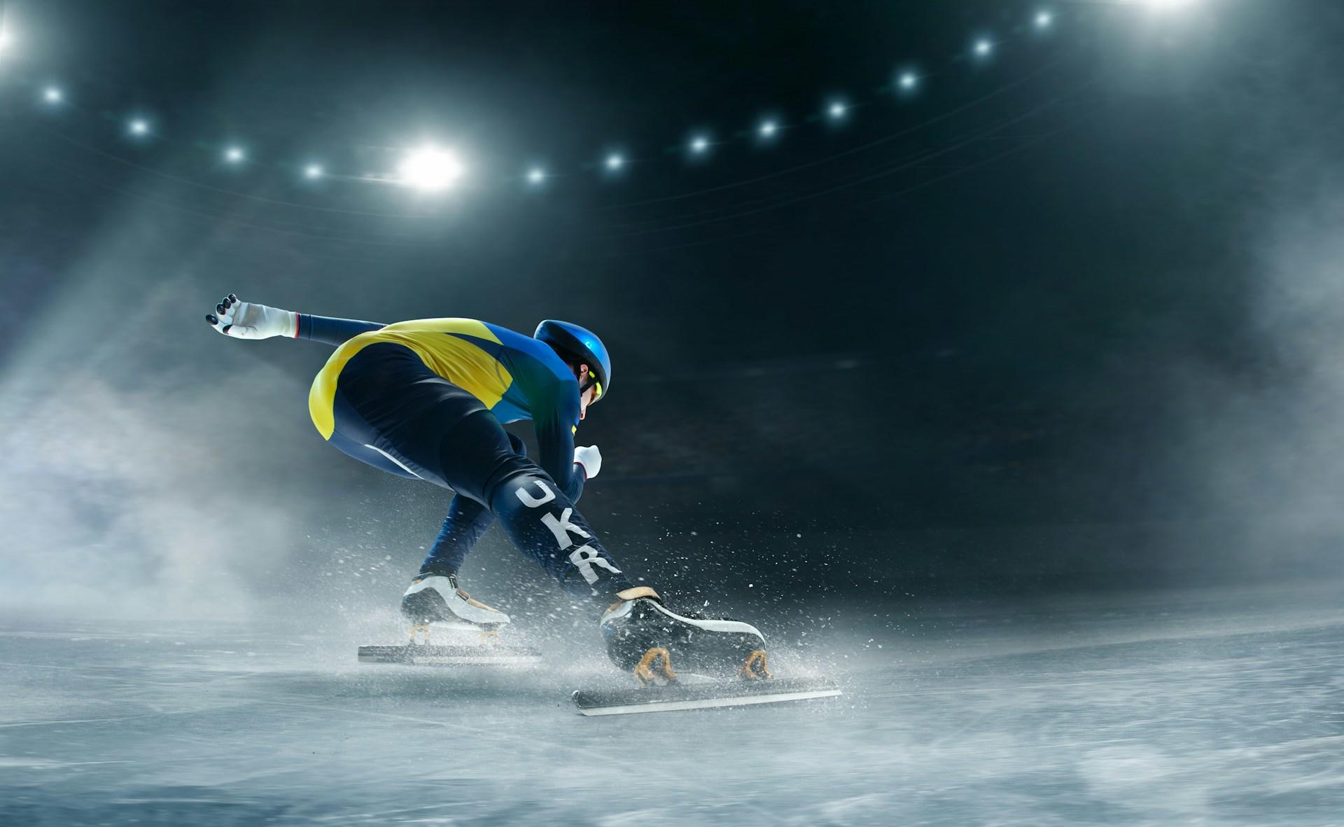 A speed skater mid-race on an ice rink under bright lights.