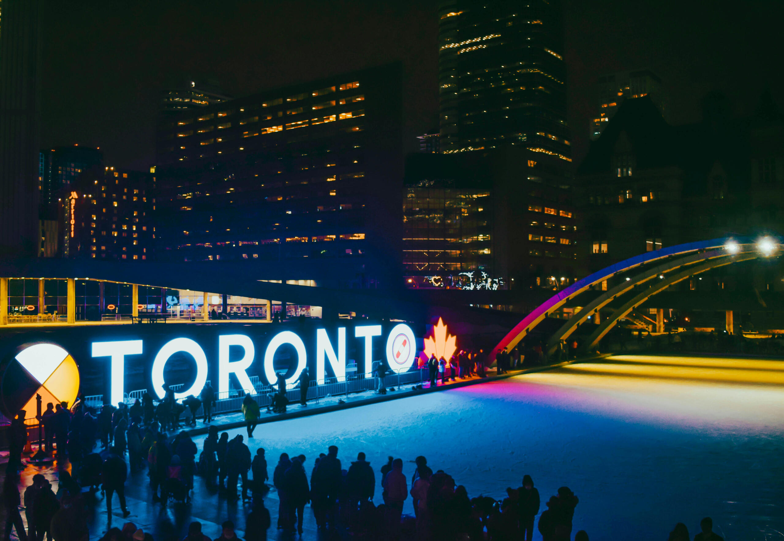 The Toronto sign light up. An ice rink is at the front, lit in different colours.
