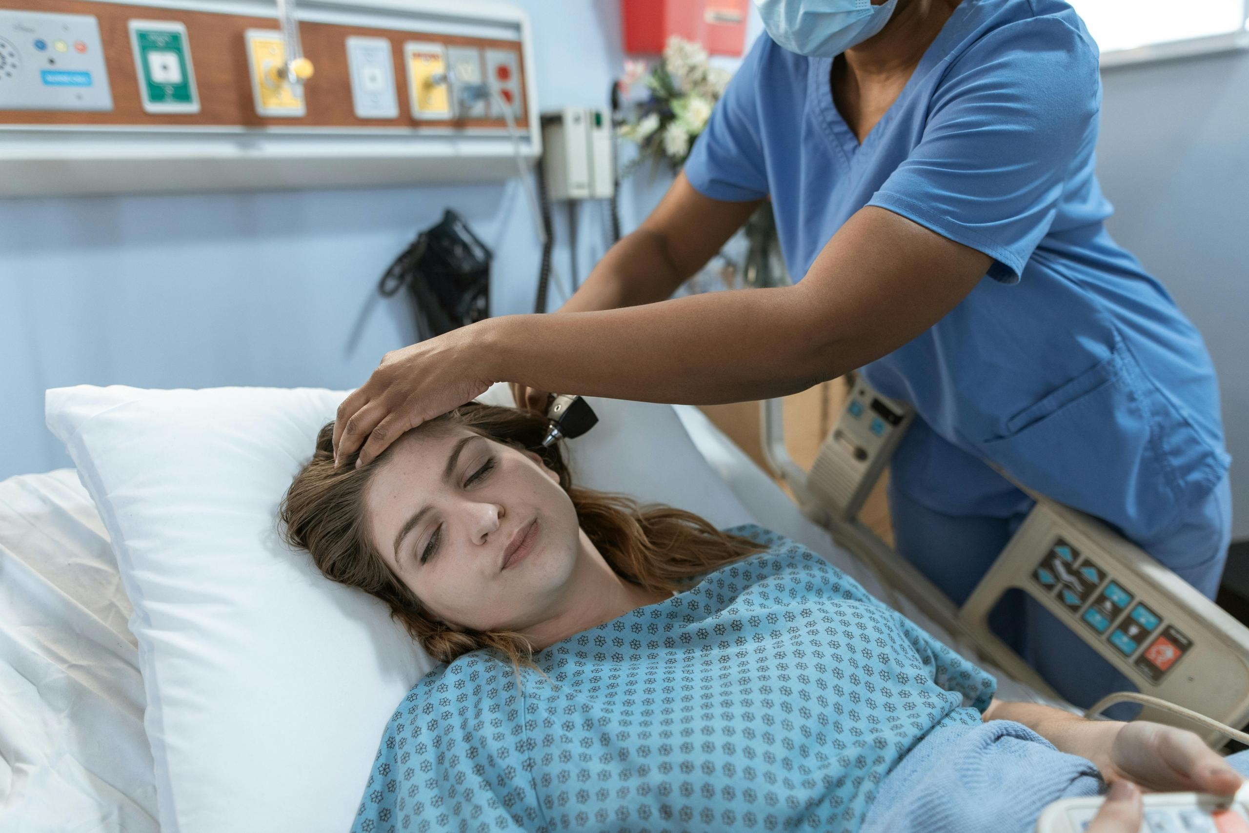A NP checking the forehead of their patient in bed at the hospital.