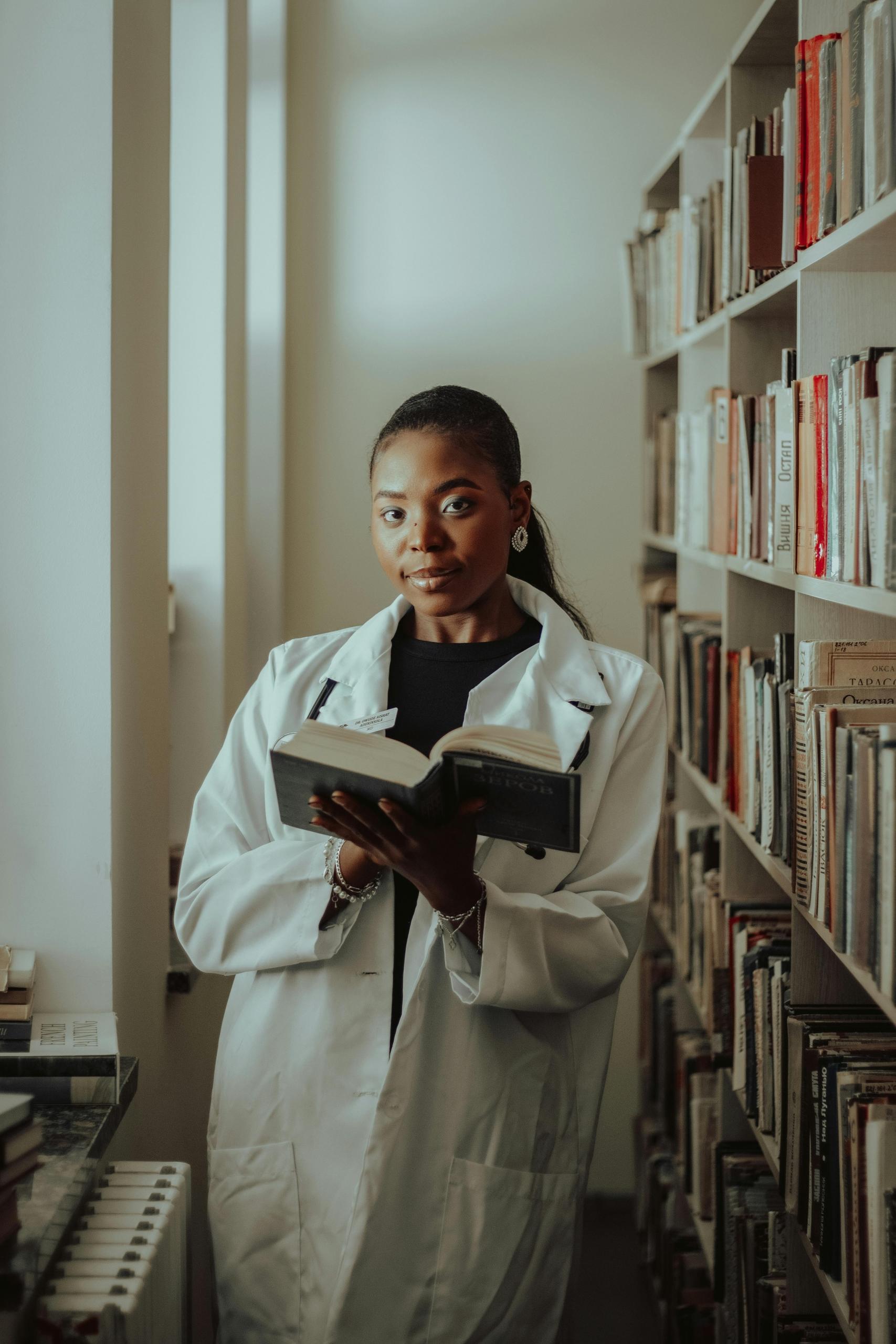 a woman readinga book in a library. She wears a lab coat with her hair tied back