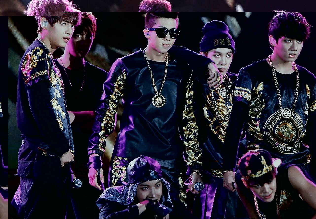 A dynamic dance performance featuring male artists in stylish, embellished black outfits with gold accents and large jewelry.