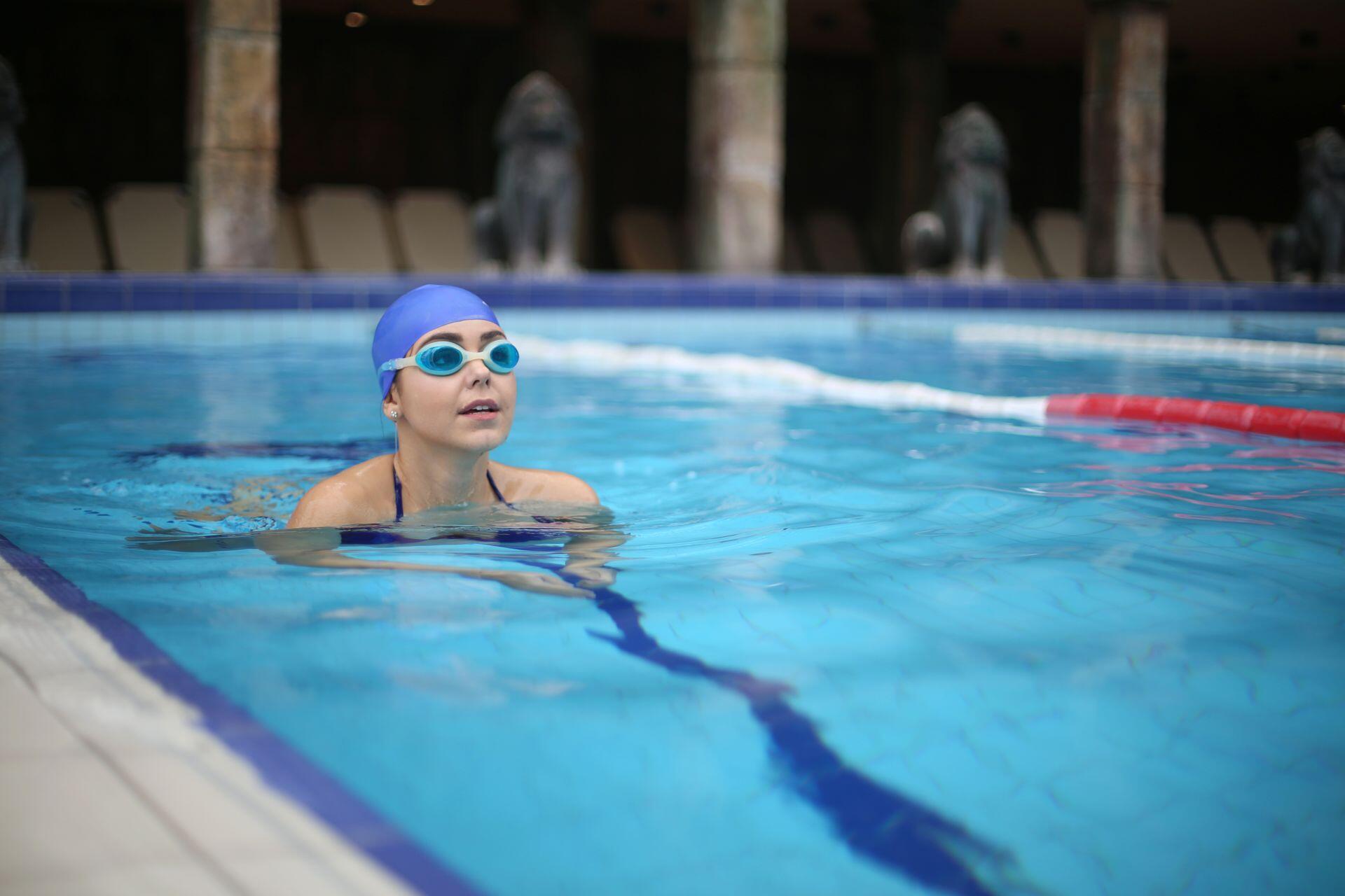 A swimmer wearing a blue cap and goggles floats in an indoor pool beside a red-and-white lane divider.