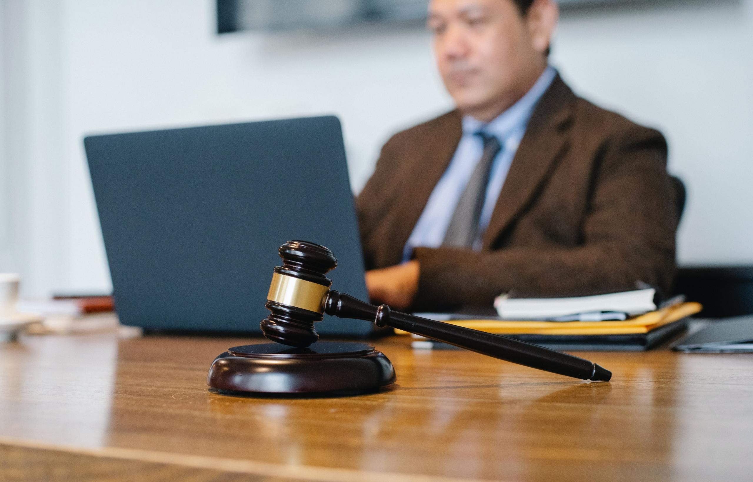 A lawyer at work on his computer, we see a gavel at the forefront of the image.