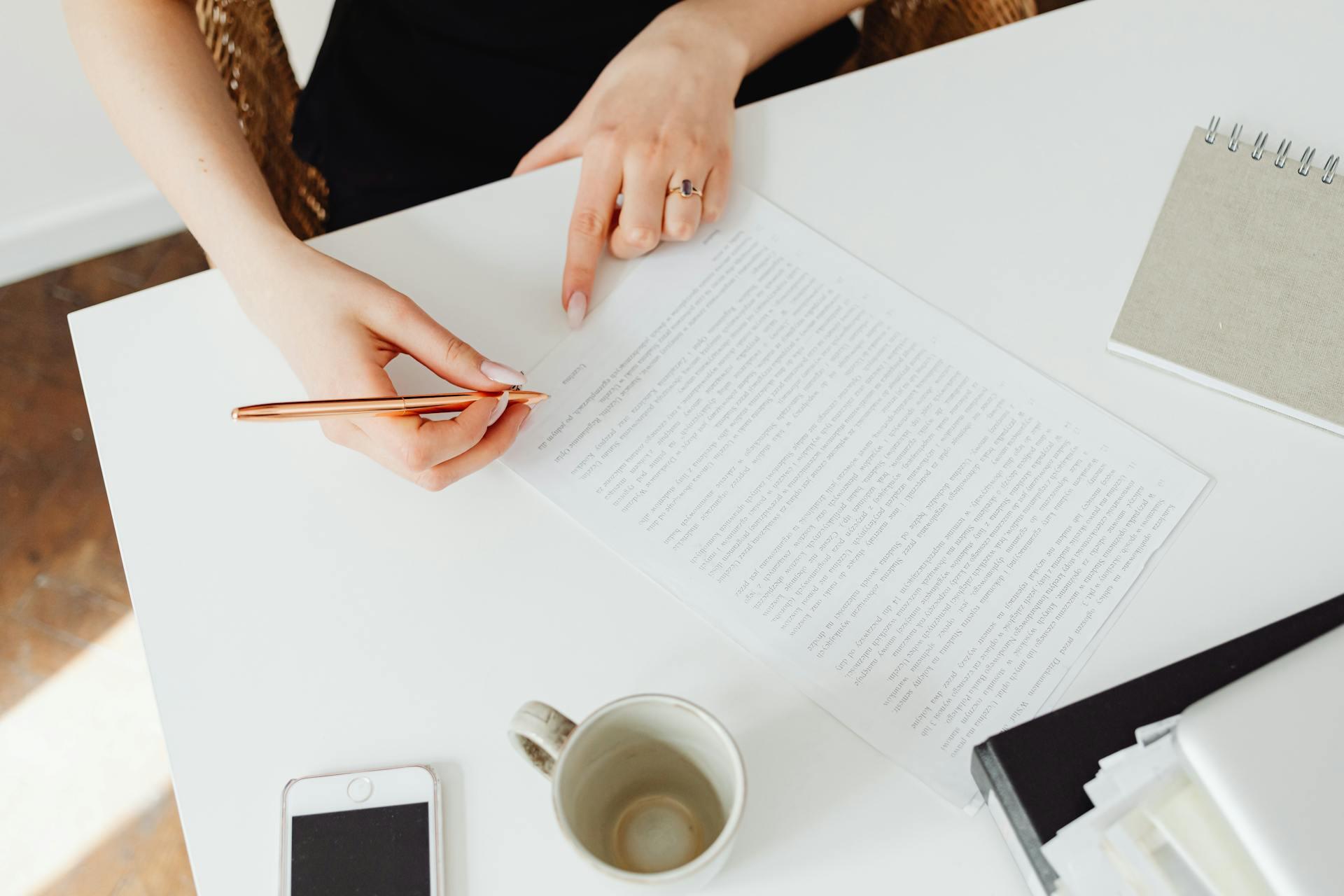 Person reviewing a document at a white desk with a pen, coffee cup, and smartphone.