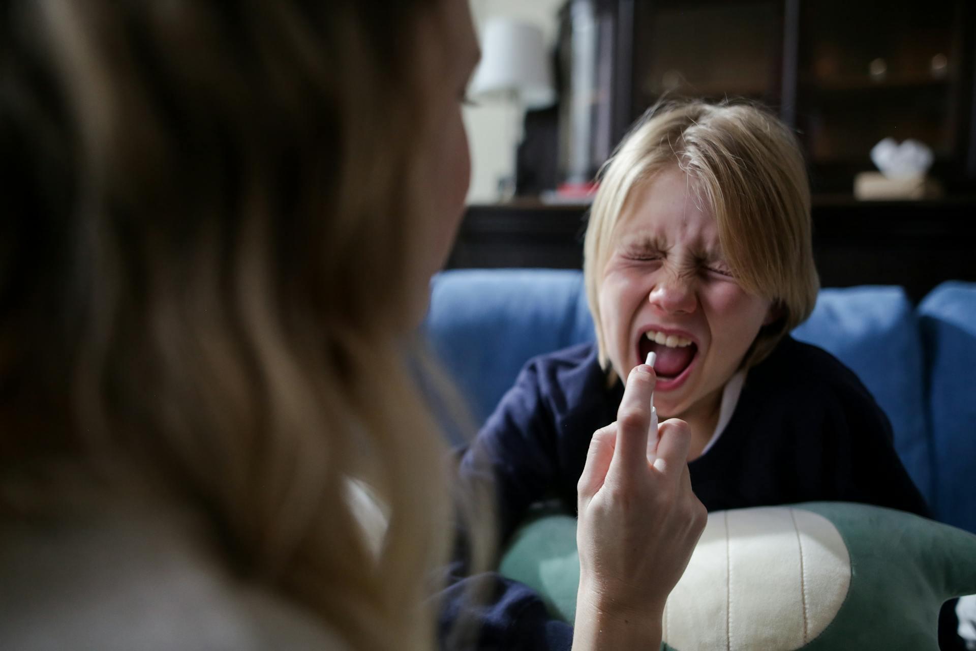 Child pretending to be sick and receiving medicine from his mother at their home.