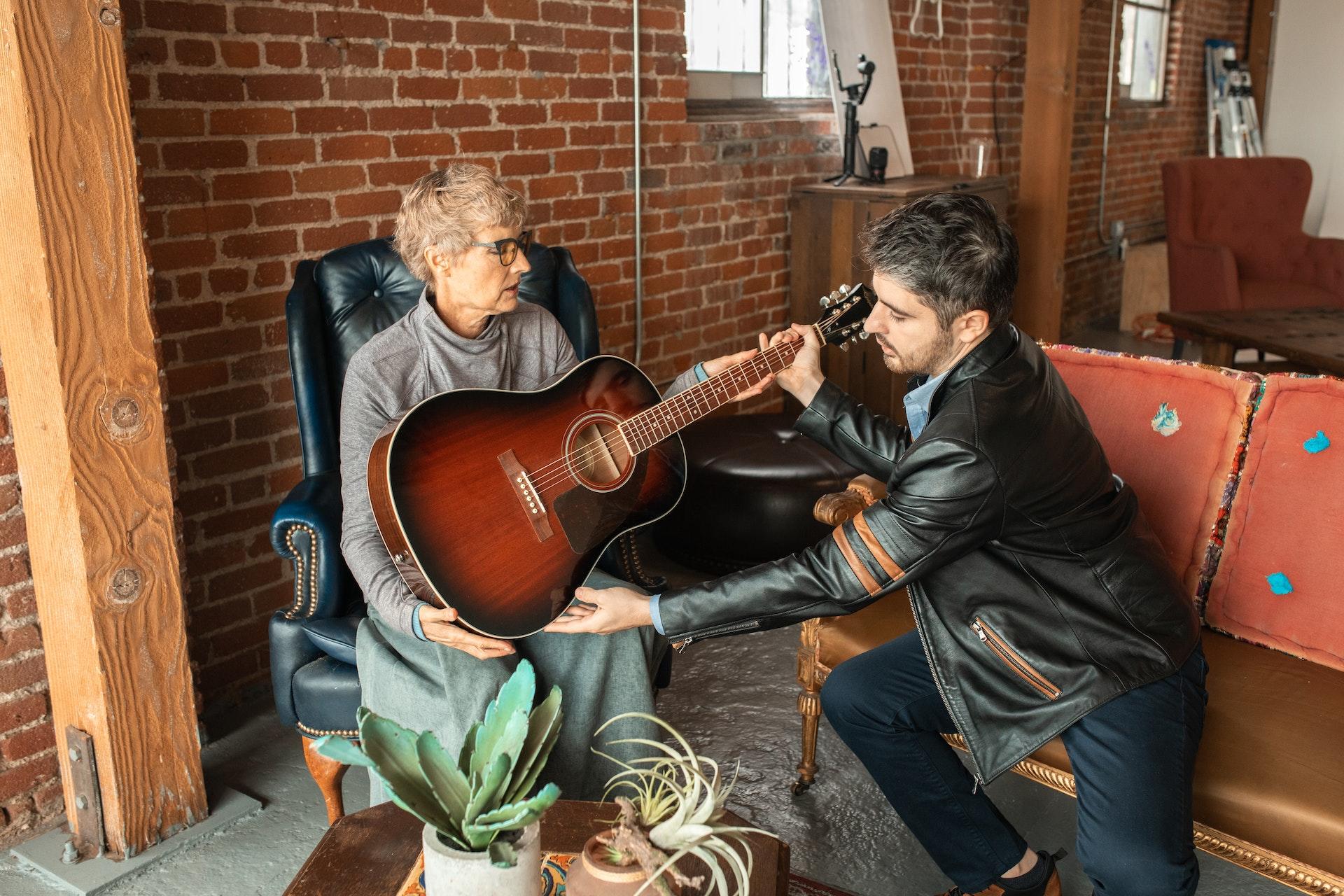 man teaches old women how to play guitar