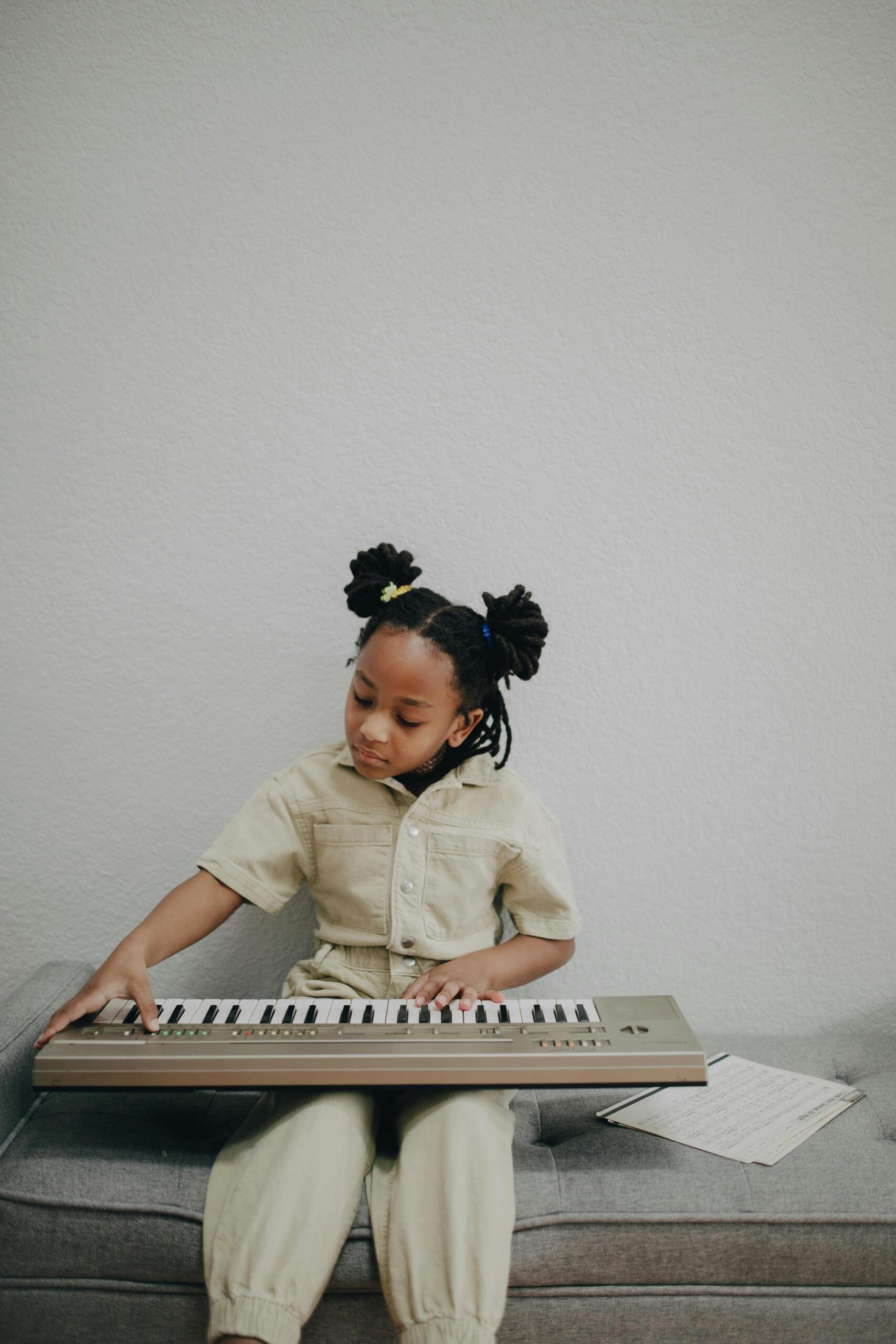 A young girl practices piano on an electronic keyboard. She sits beside sheet music. Source: PNW Production.