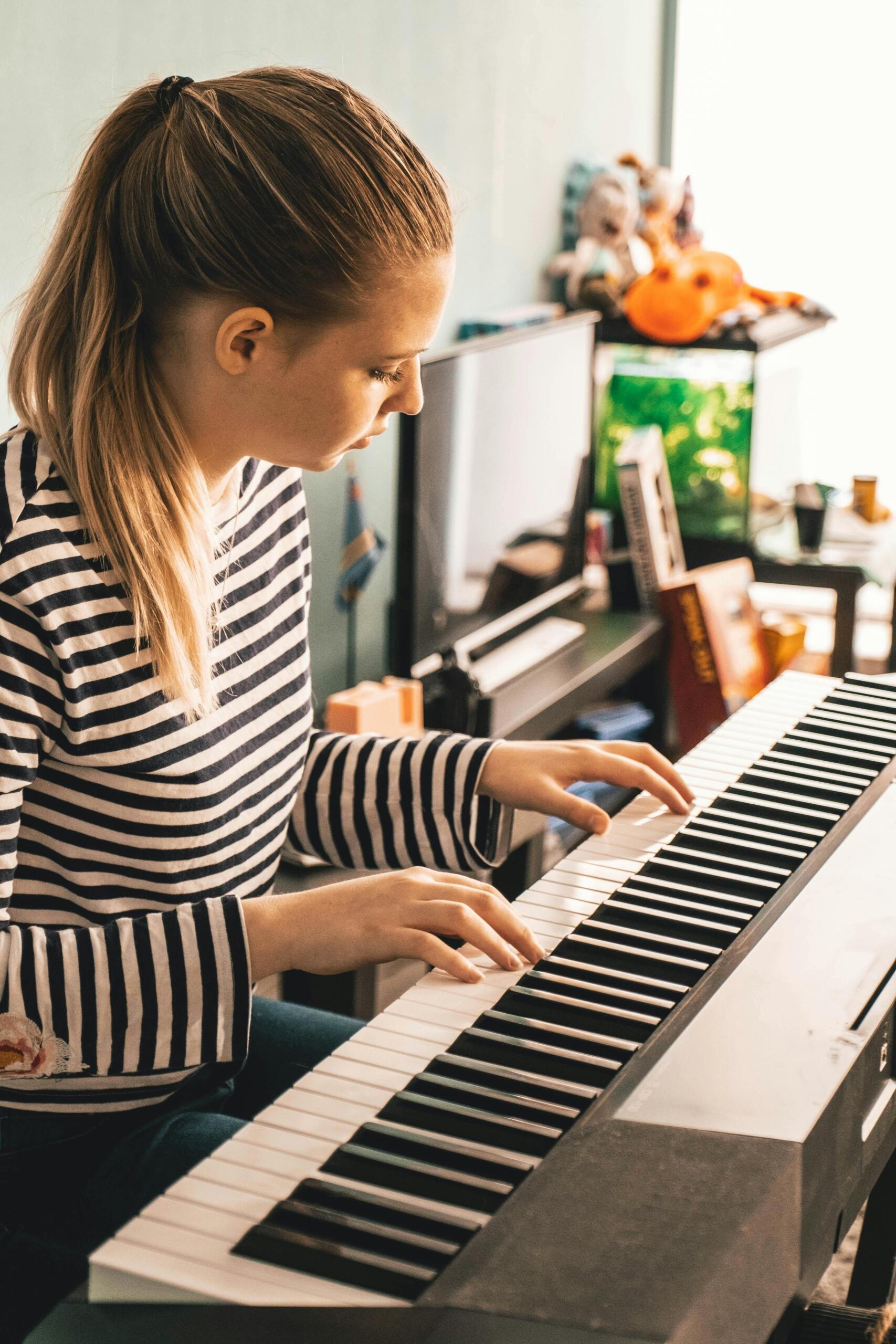 A teenage girl in a striped shirt plays a keyboard.