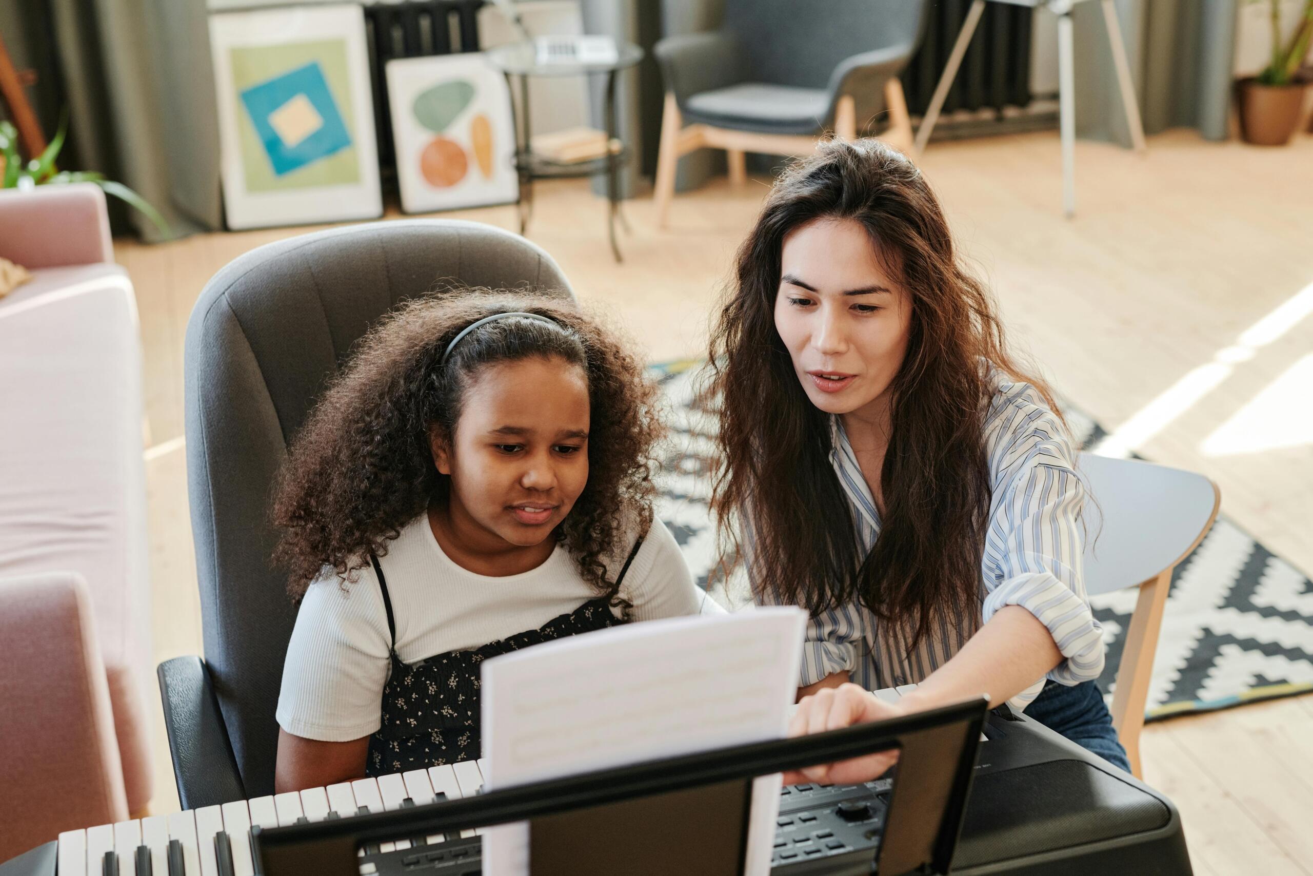 A piano teacher helps a student read music at the keyboard.