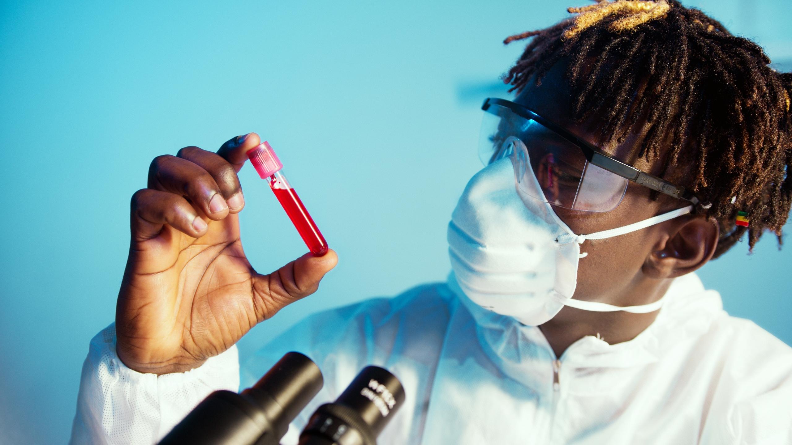 A chemist examins a test tube containing red liquid.