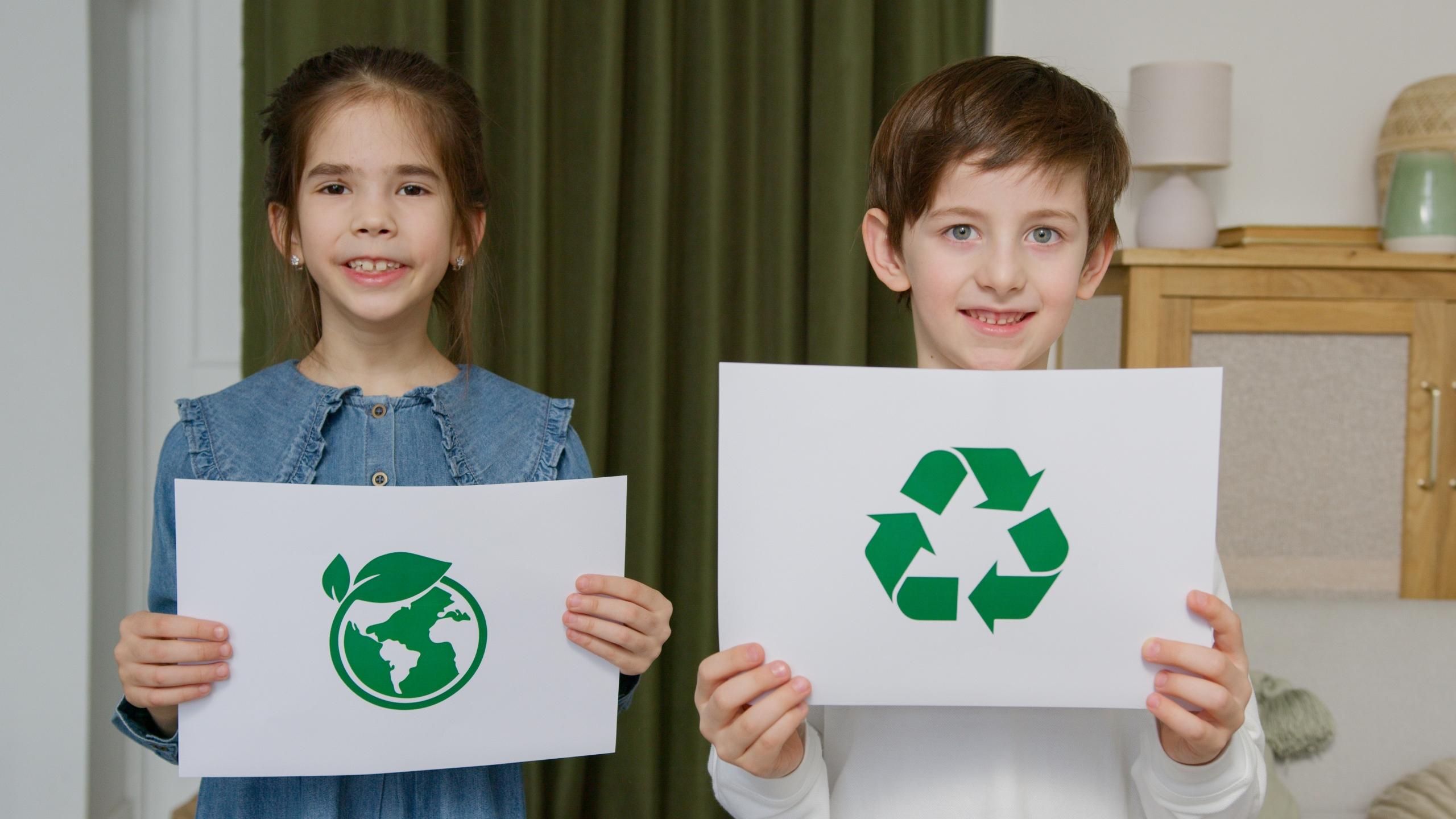 two children hold papers with recycling symbols on them.